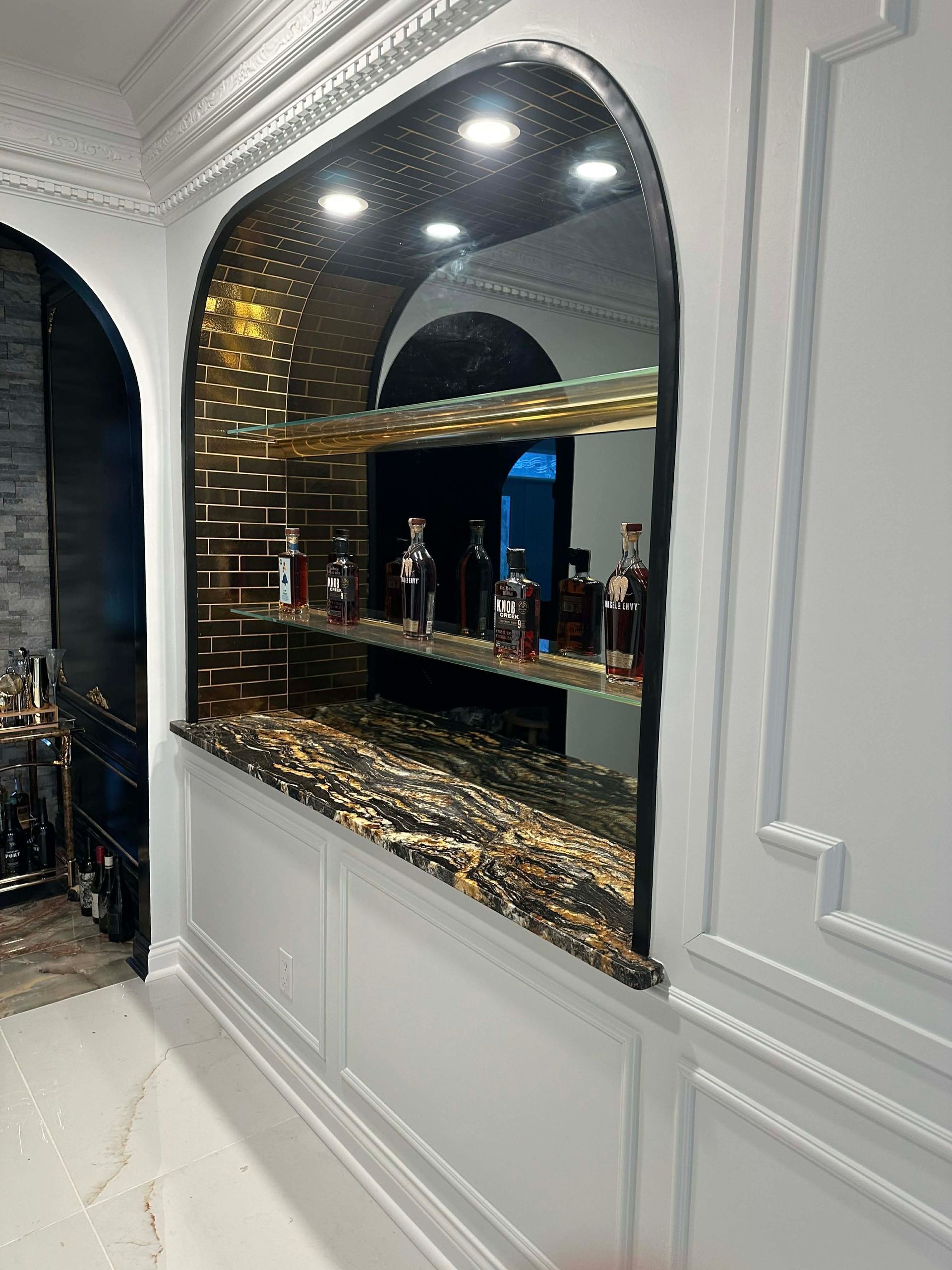 Elegant black arched bar with bottles and glass shelves in a white paneled room