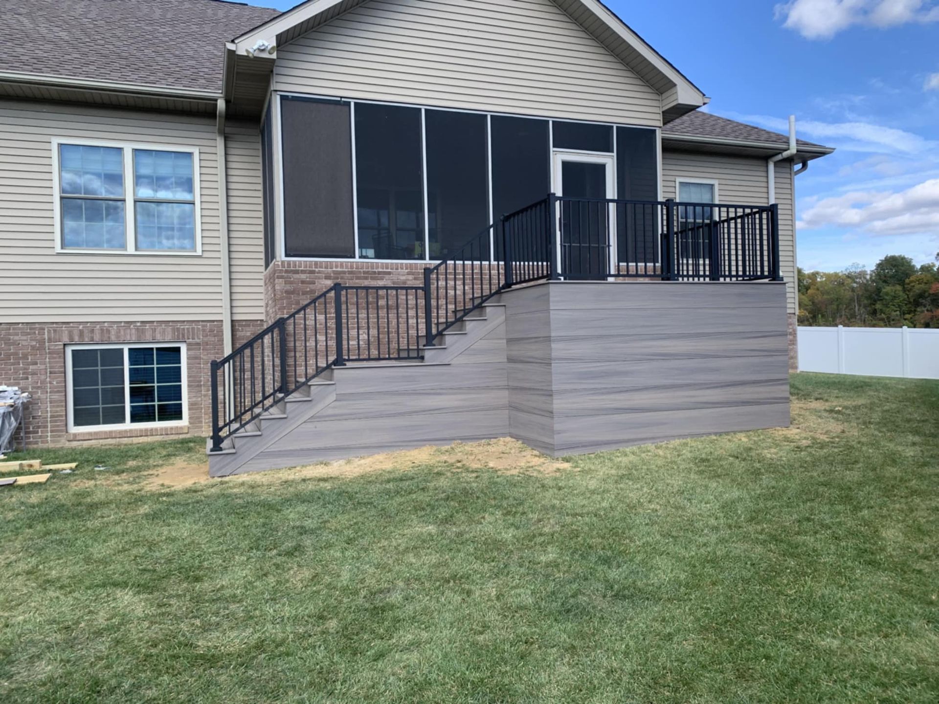 Backyard deck with black railings, gray skirting, and screened porch attached to a beige house