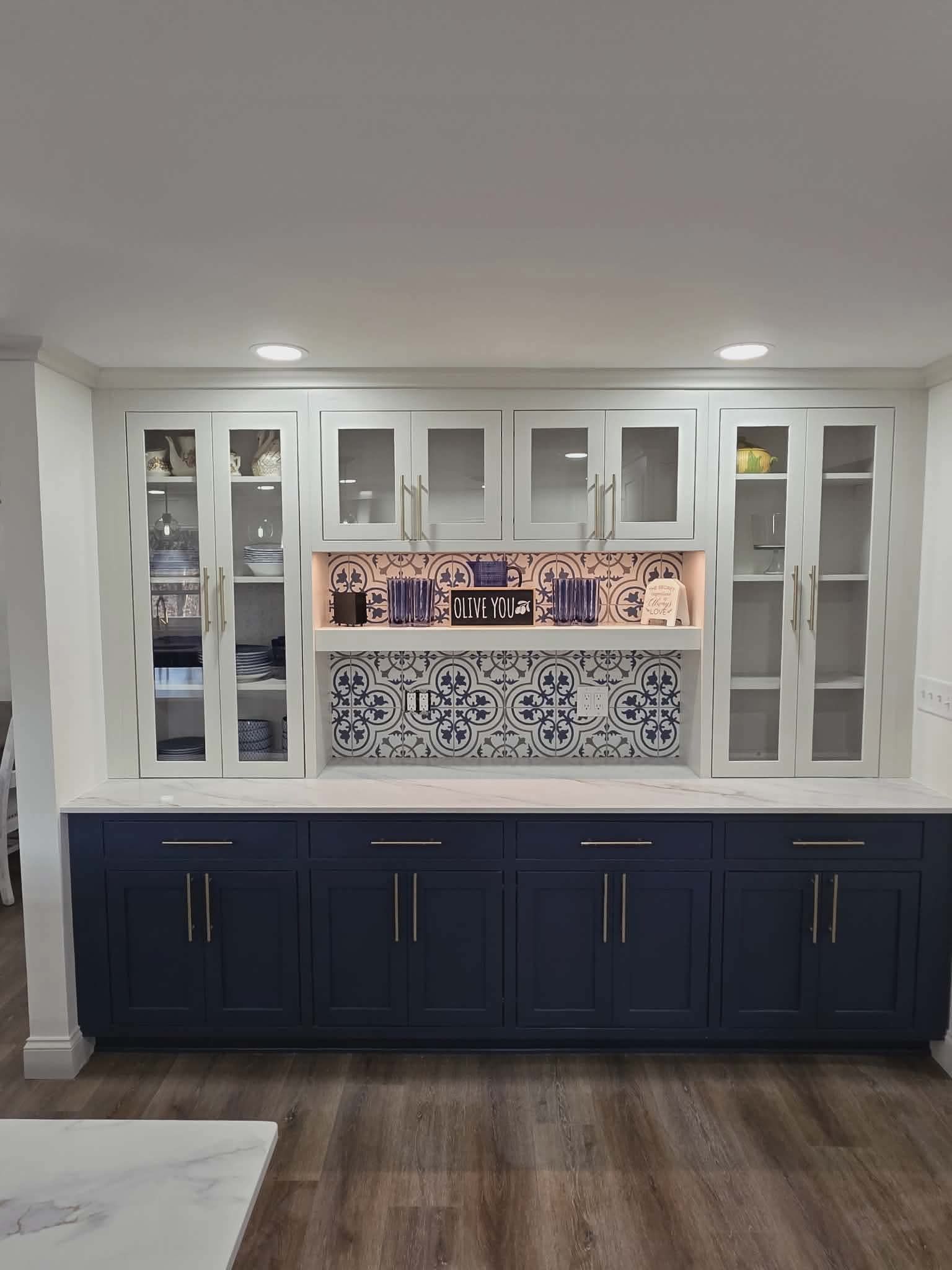 Built-in white cabinets with glass doors above a navy lower cabinet and decorative tile wall.