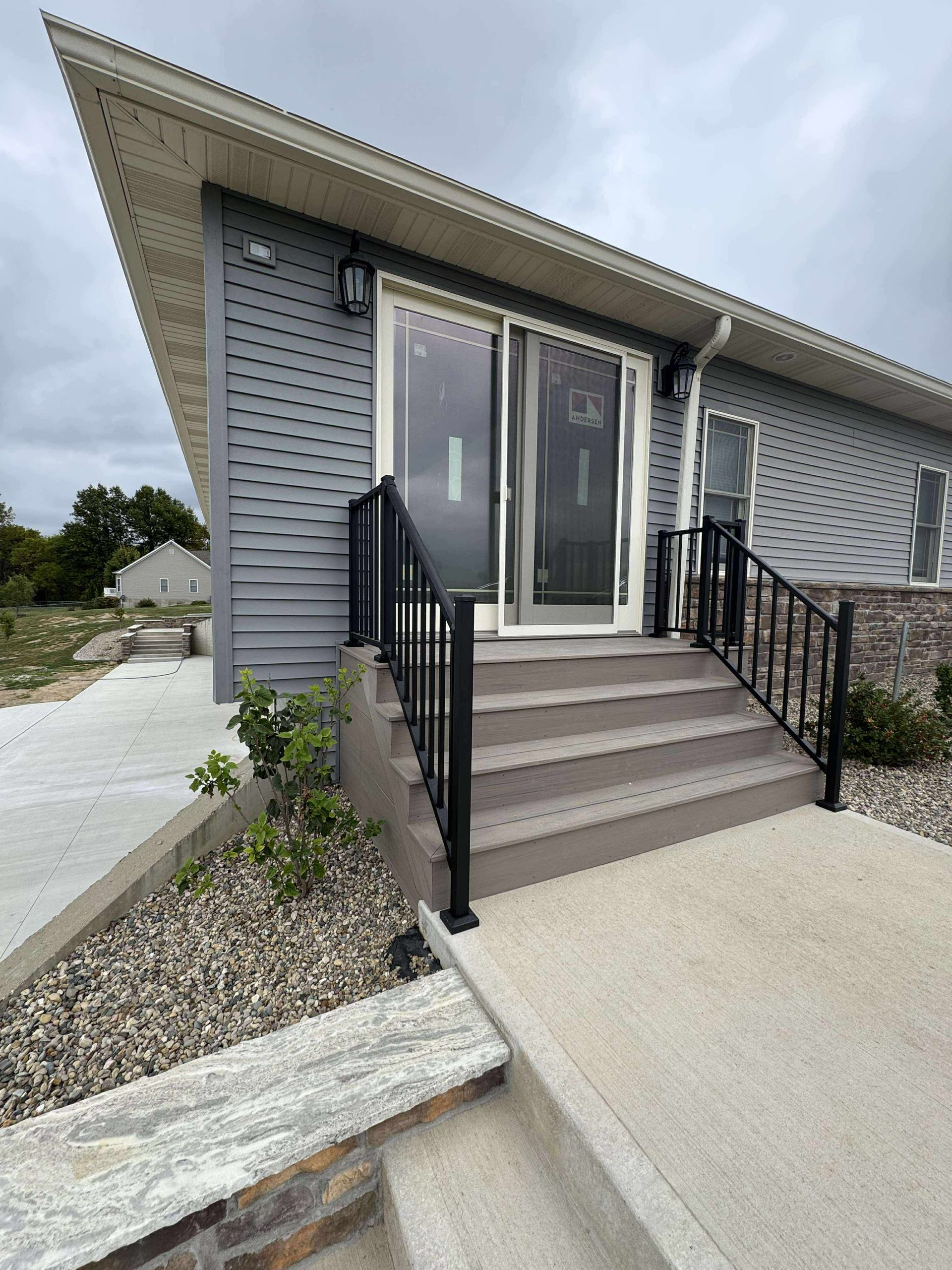Modern building entrance with steps, black railings, and double glass doors in a gray exterior.