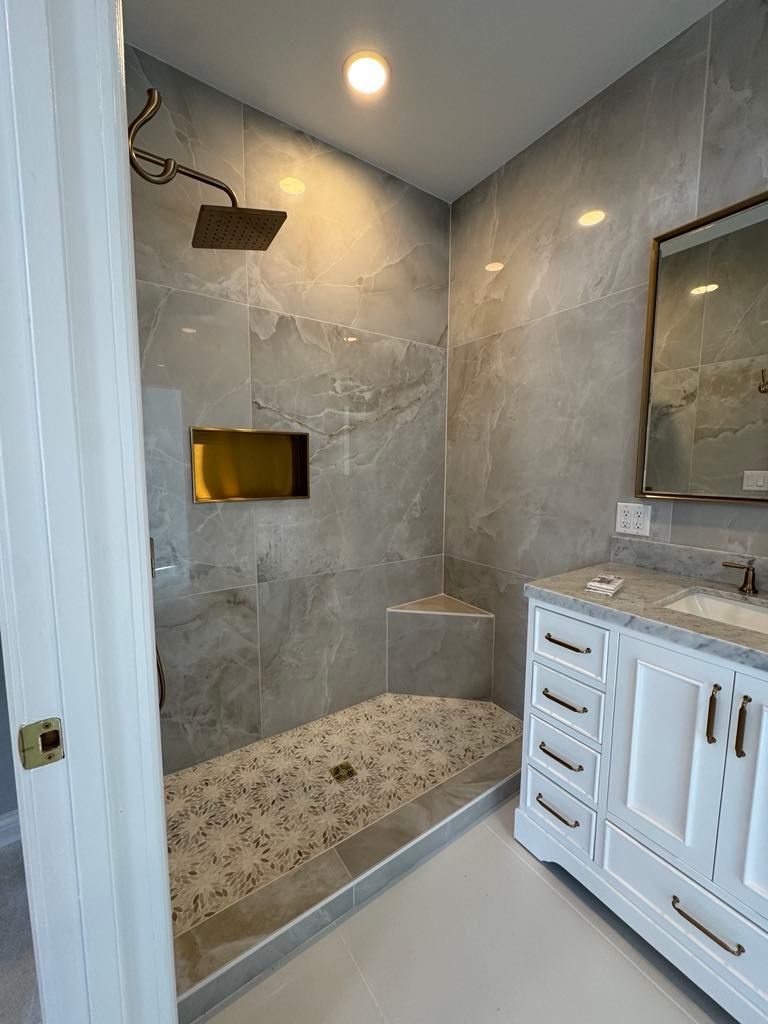 Modern marble-tiled shower with glass enclosure, brass fixtures, and white vanity in a bathroom