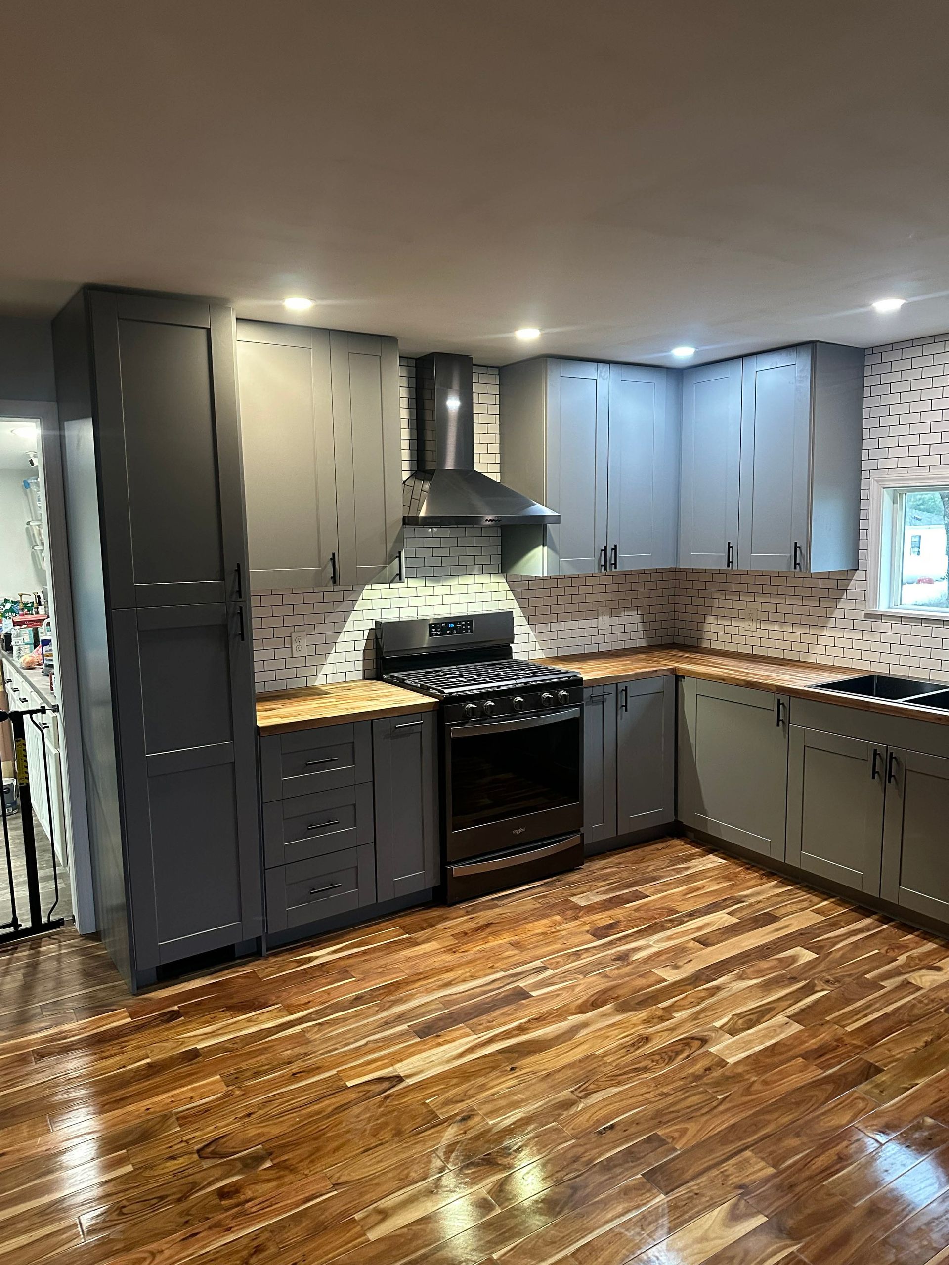 Modern kitchen with dark cabinets, black stove, tile backsplash, and wood floors