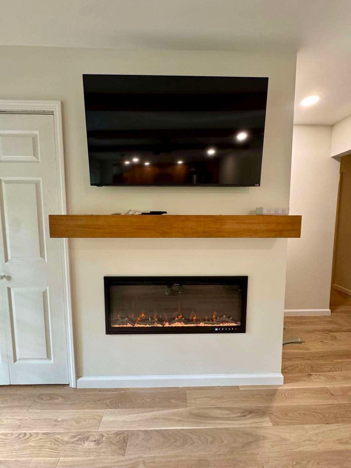 Modern living room wall with mounted TV, long wooden mantel, and built-in electric fireplace.