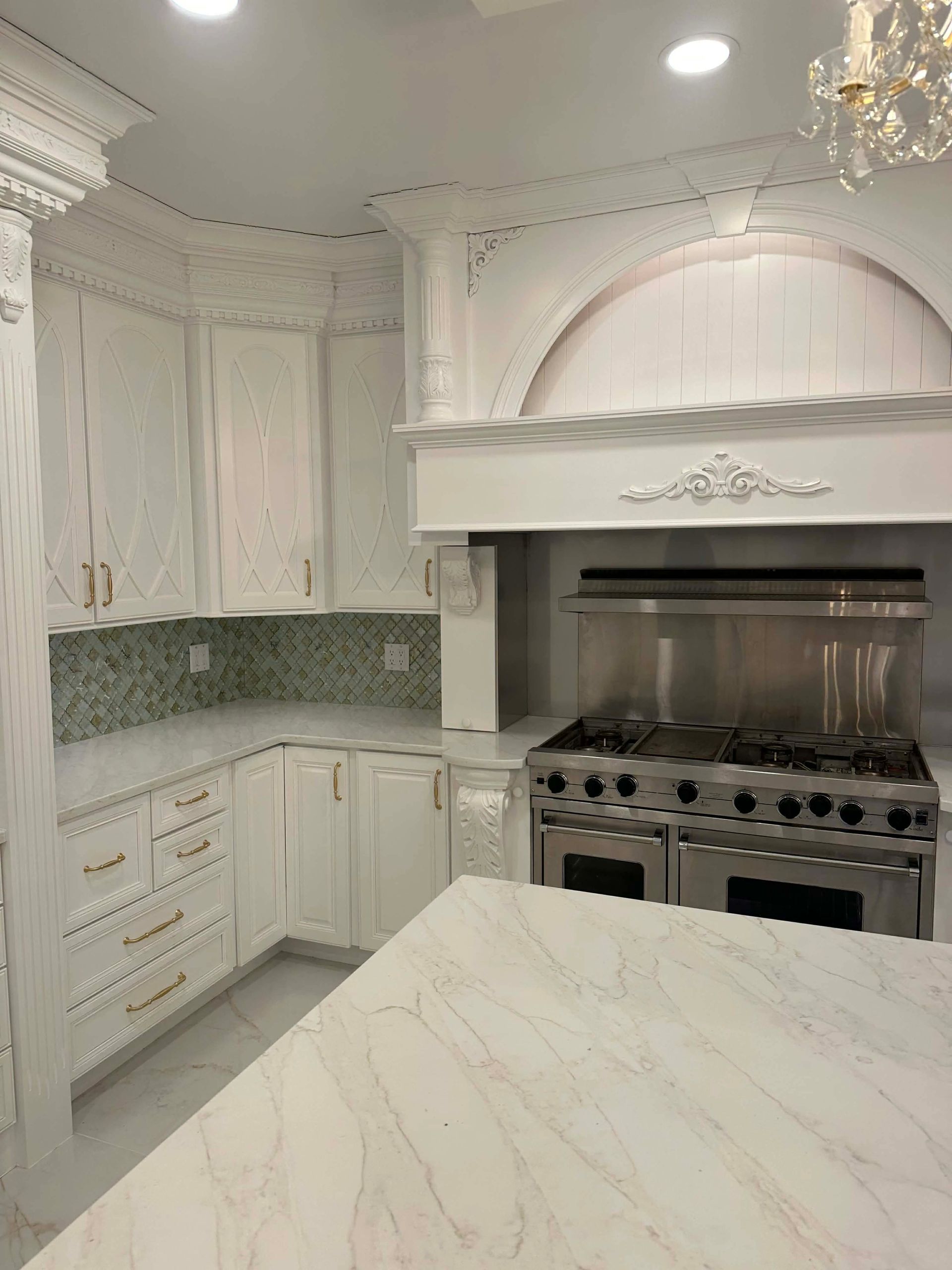 Elegant white kitchen with marble island, ornate cabinets, and stainless steel range hood