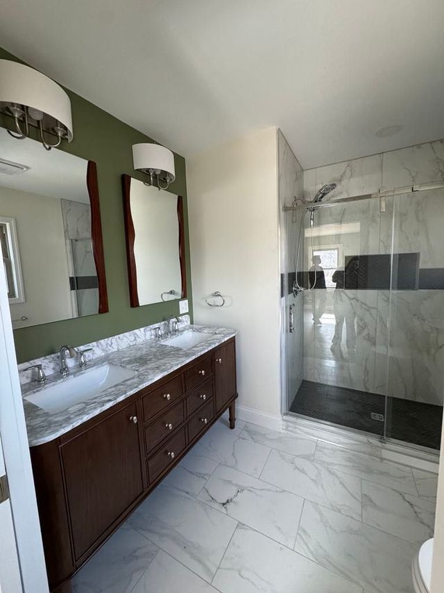 Modern bathroom with marble tile shower, dark wood vanity, and large mirrors under wall sconces