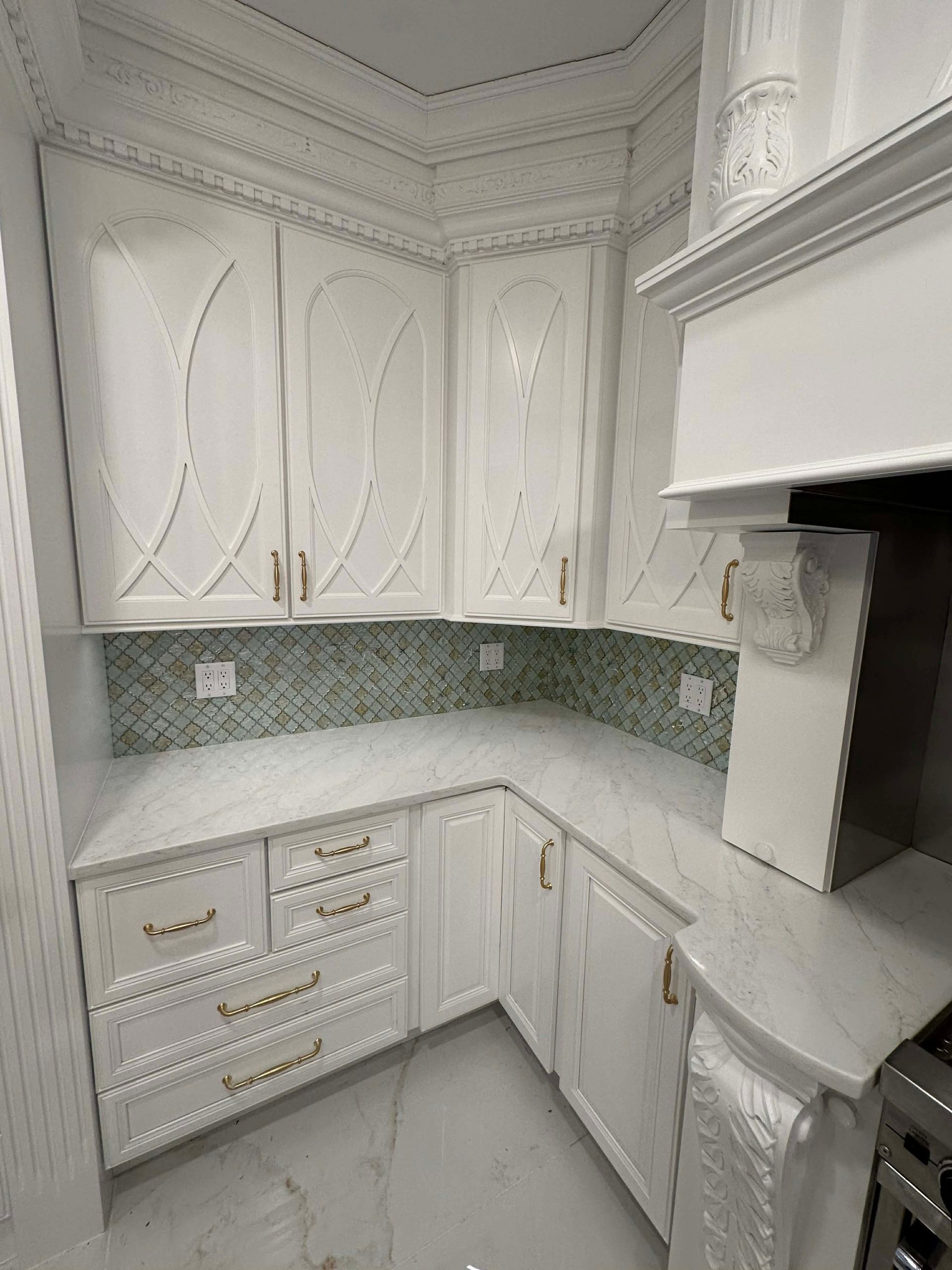 White ornate kitchen with green mosaic backsplash, marble countertops, and built-in cabinetry