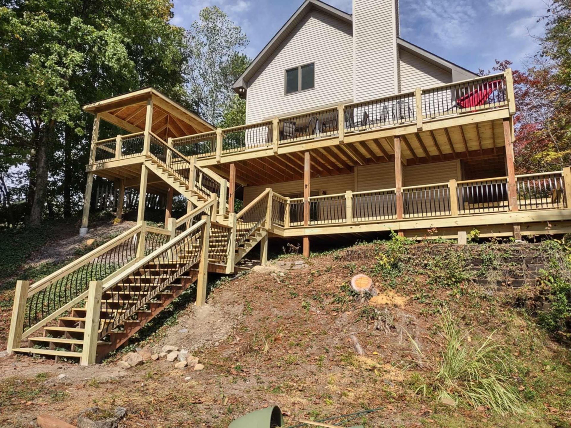Wooden house deck with stairs and railing on a wooded hillside under a clear sky