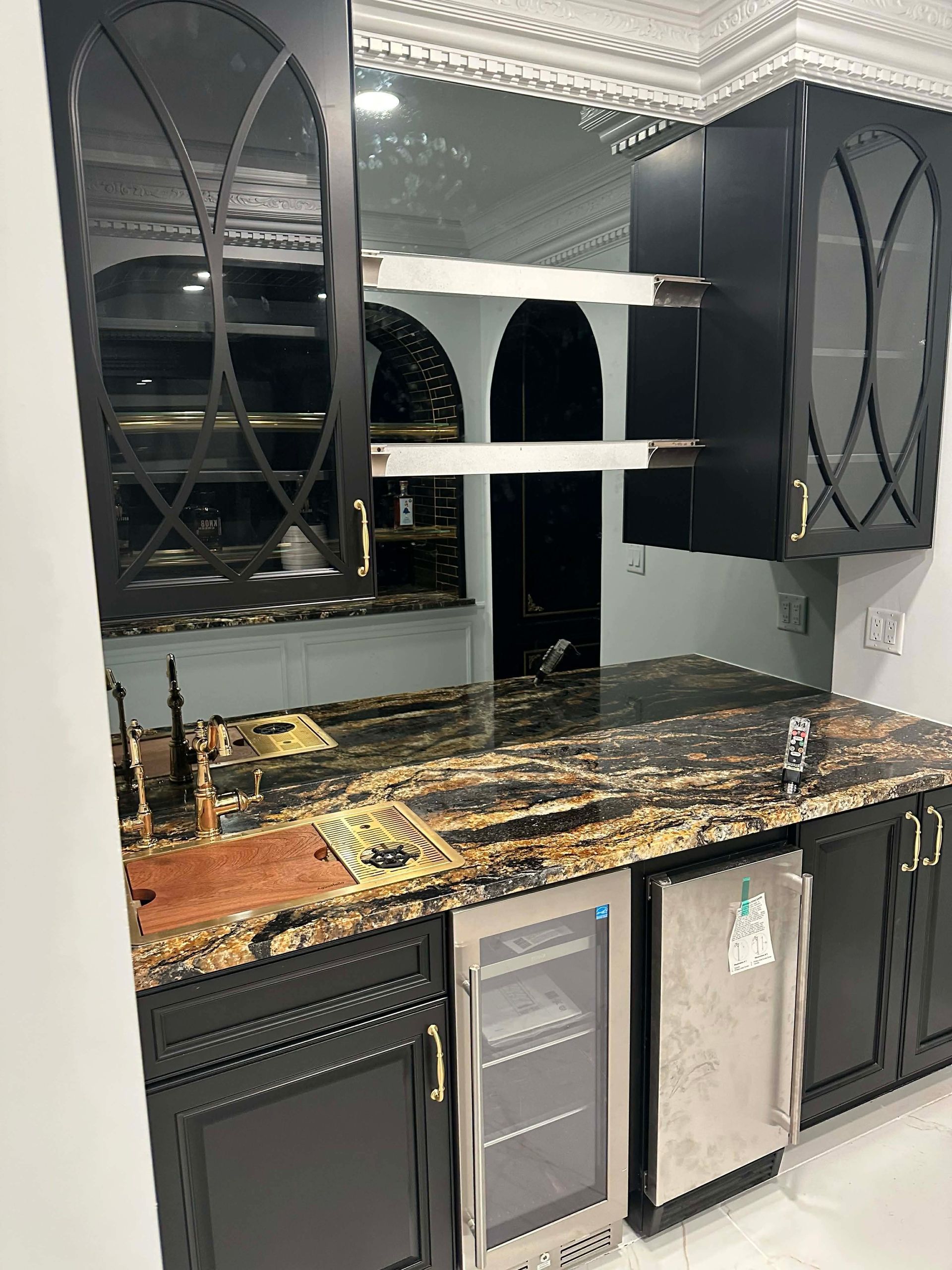 Black-and-gold kitchen with mirrored cabinets, marble countertop, and two mini fridges beneath the counter