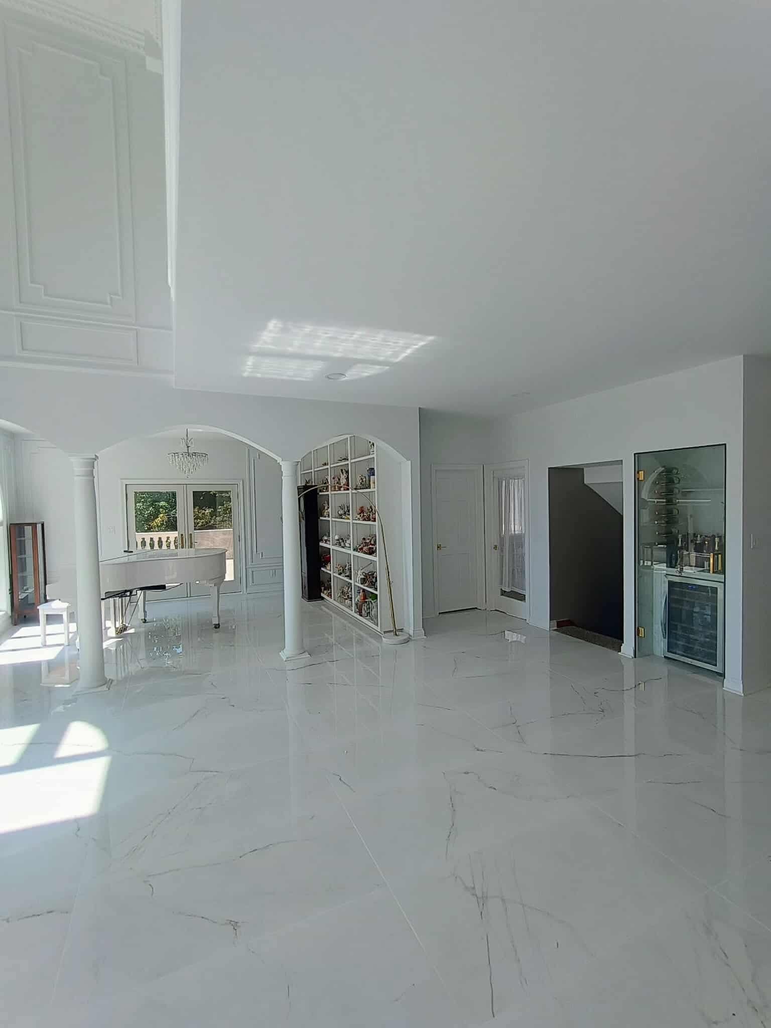 Bright white modern living room with glossy floor, arched openings, and a glass display cabinet.