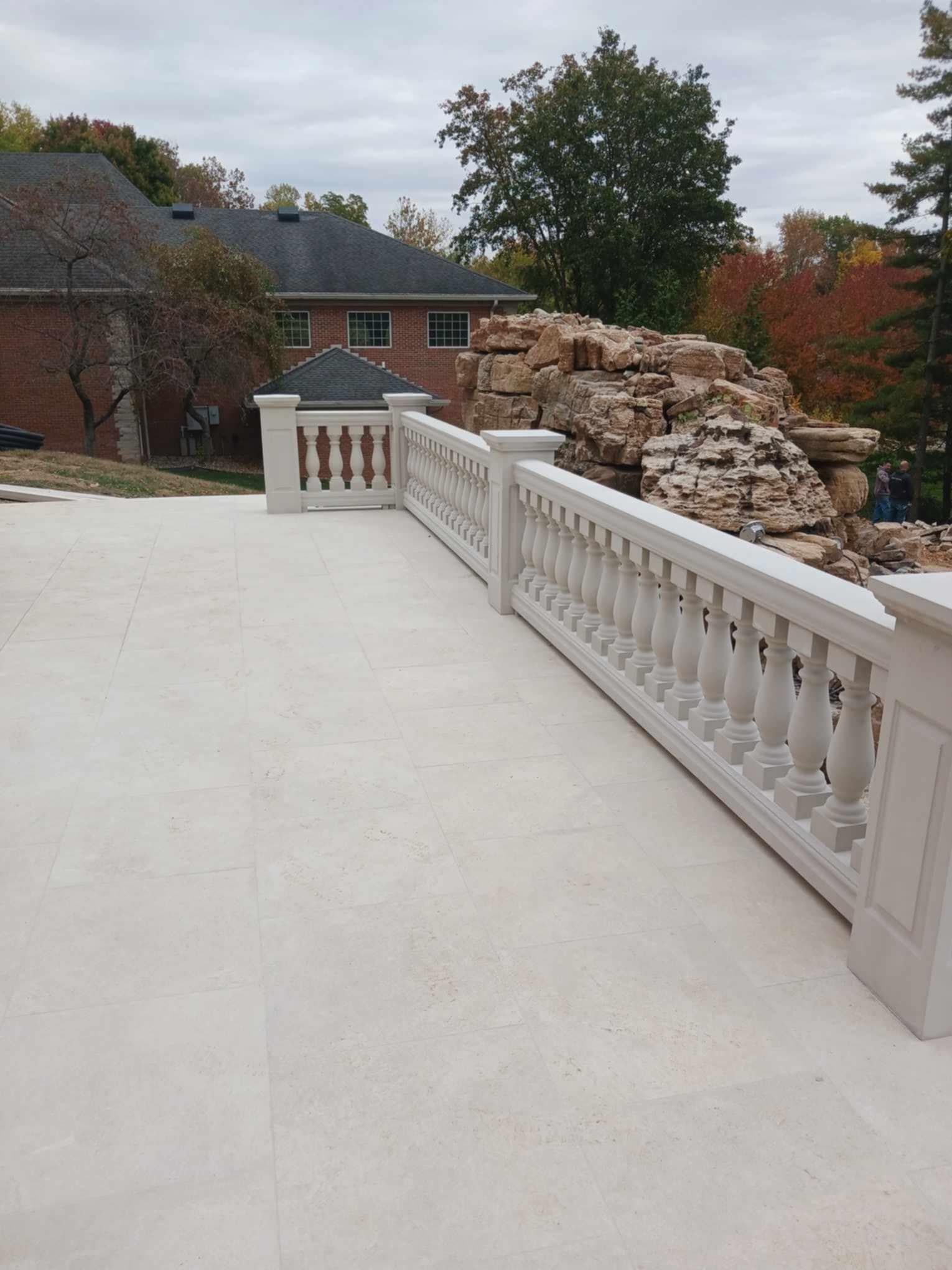 Stone terrace with white balustrade beside a landscaped rock wall and autumn trees