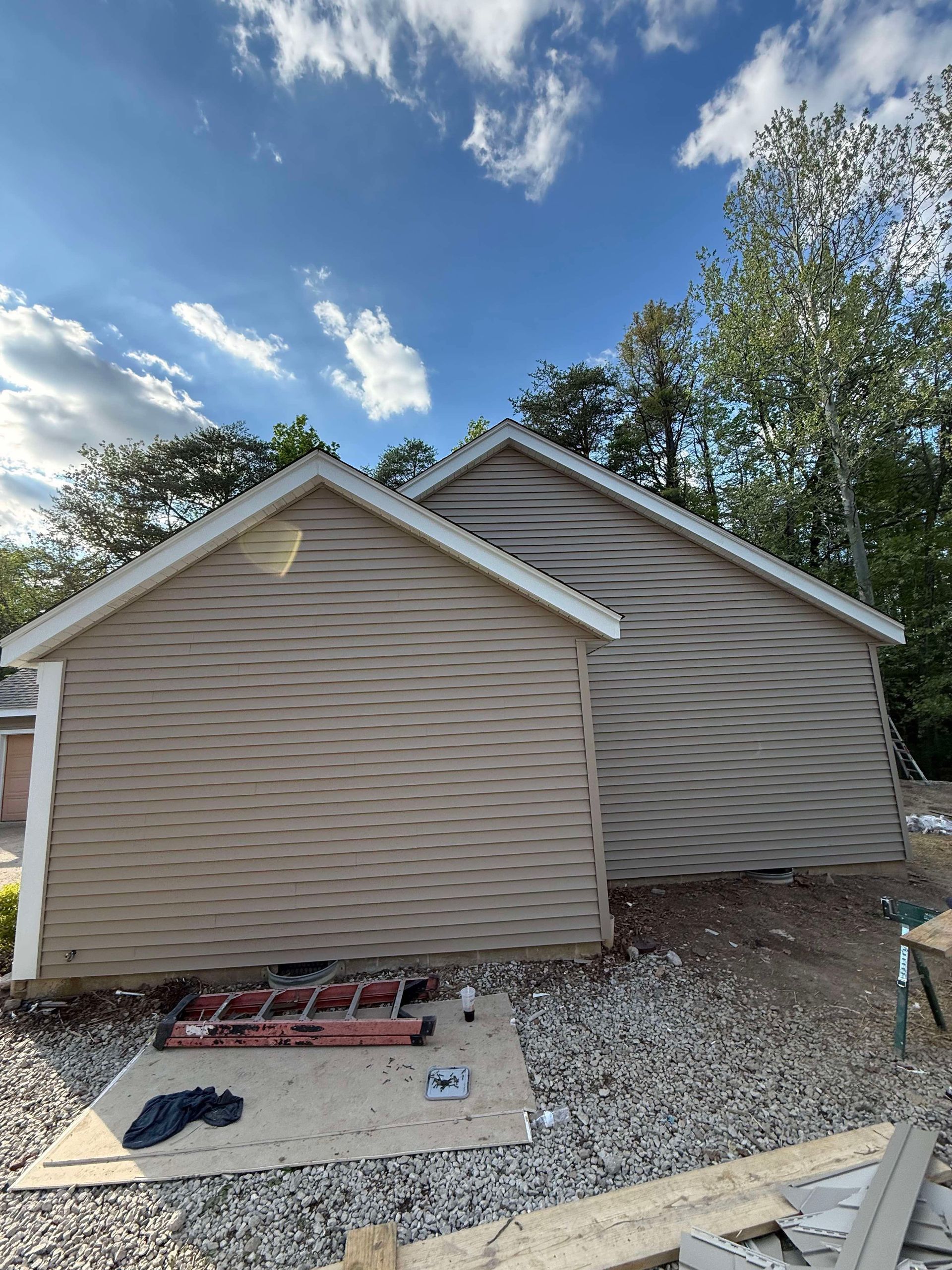 Beige house exterior with matching siding, gravel yard, and blue sky with clouds