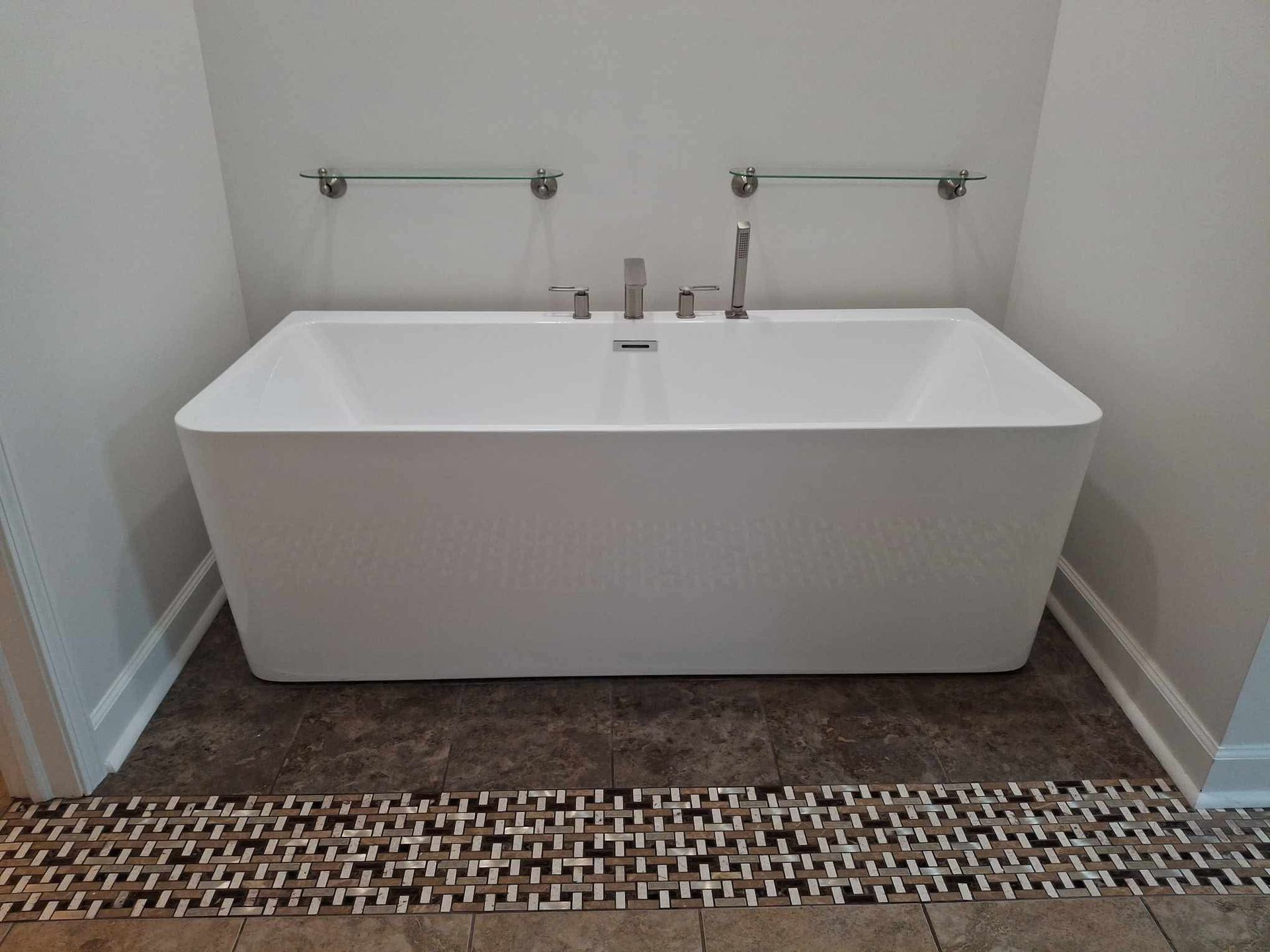 Modern freestanding white bathtub with chrome fixtures in a tiled bathroom