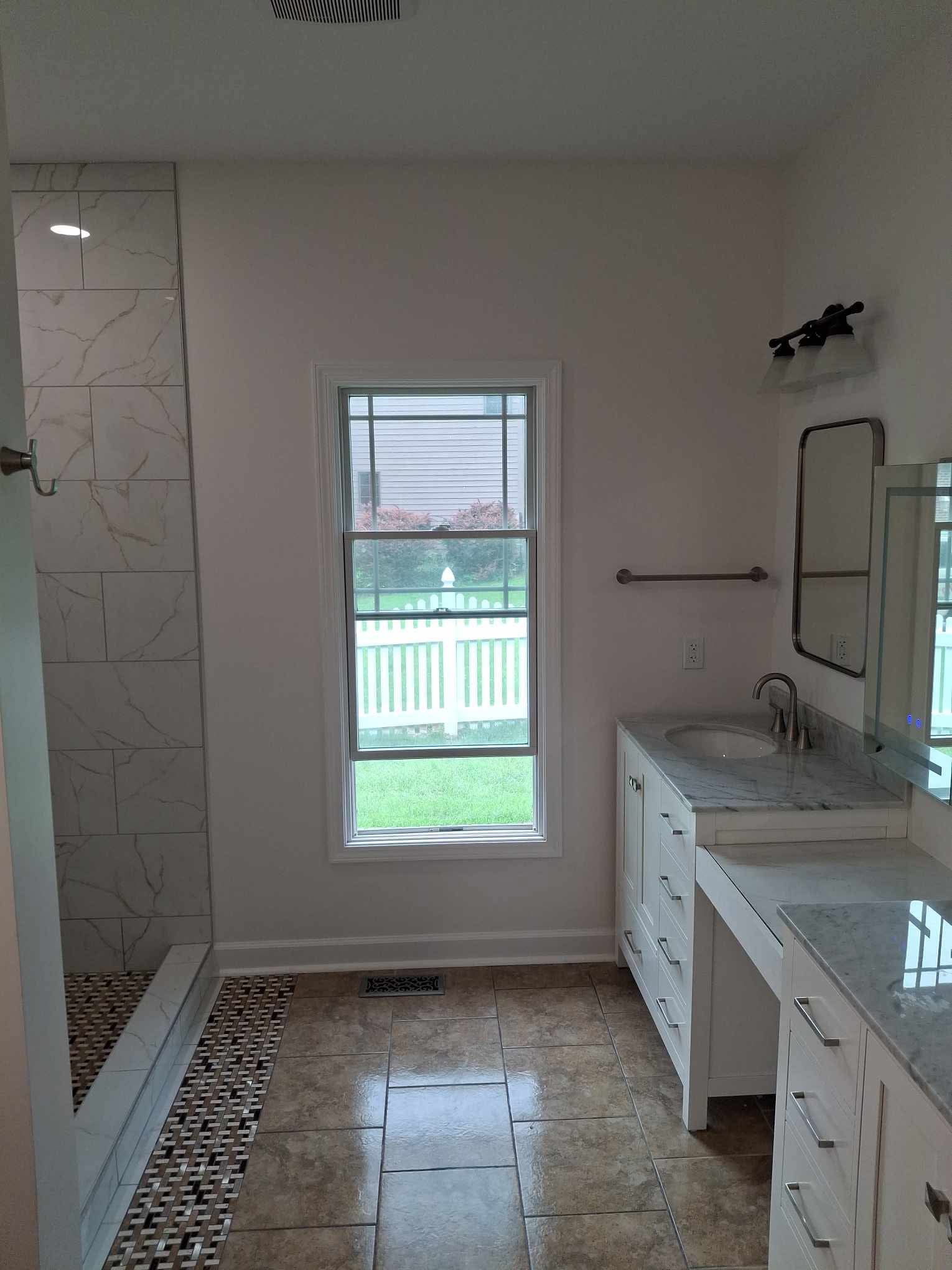 Modern bathroom with a walk-in shower, window, double vanity, and mosaic tile floor.
