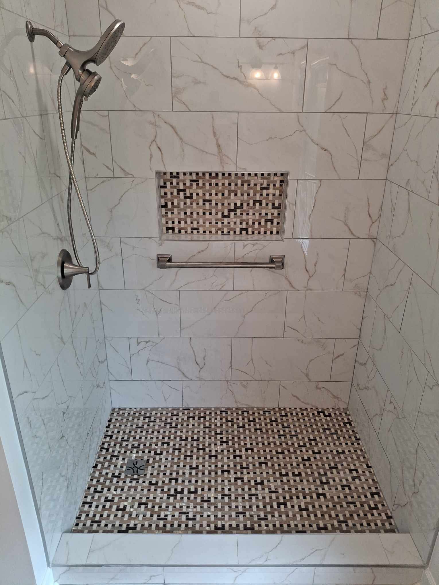 Empty tiled shower with handheld showerhead and mosaic floor and seat accents