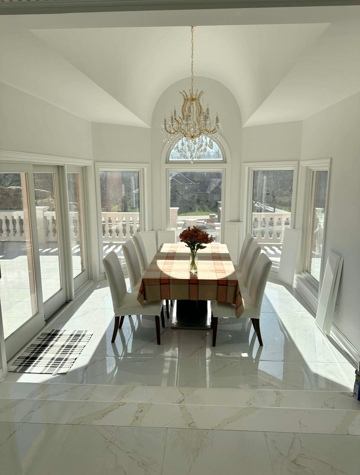 Bright sunroom dining area with a long table, white chairs, and tall windows