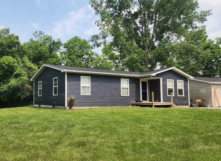 Single-story gray house with white trim and a small front porch, set on a grassy lawn with trees behind.