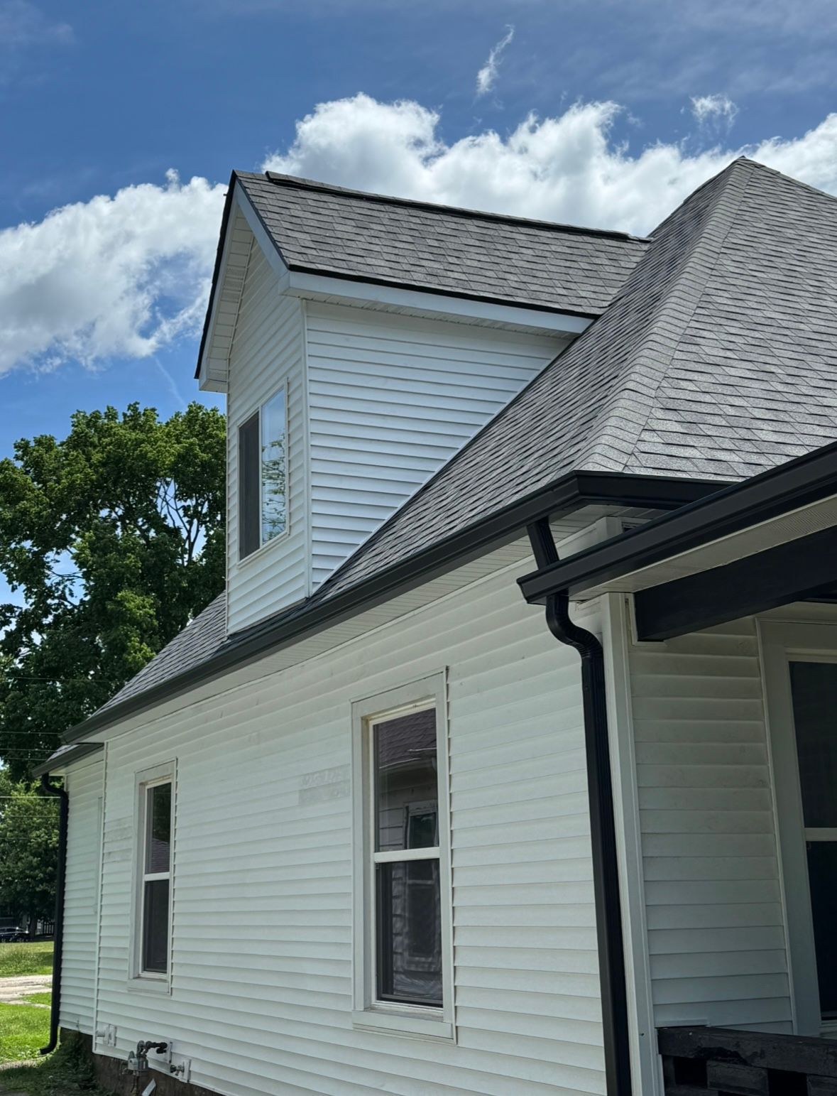 White house exterior with gray roof and black gutter under a blue sky with clouds