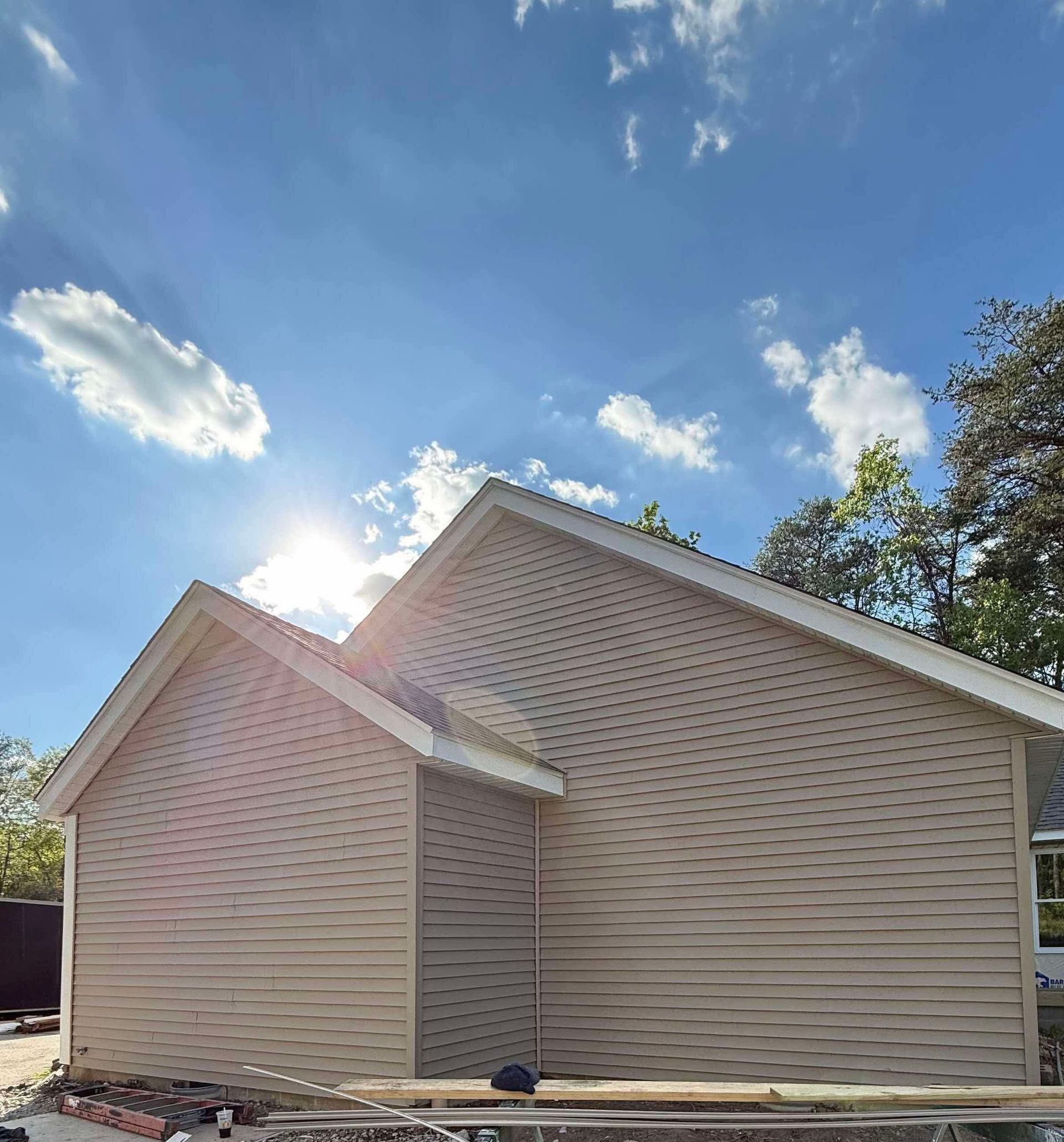 Beige house exterior with wavy siding and a steep roof under a bright blue sky.
