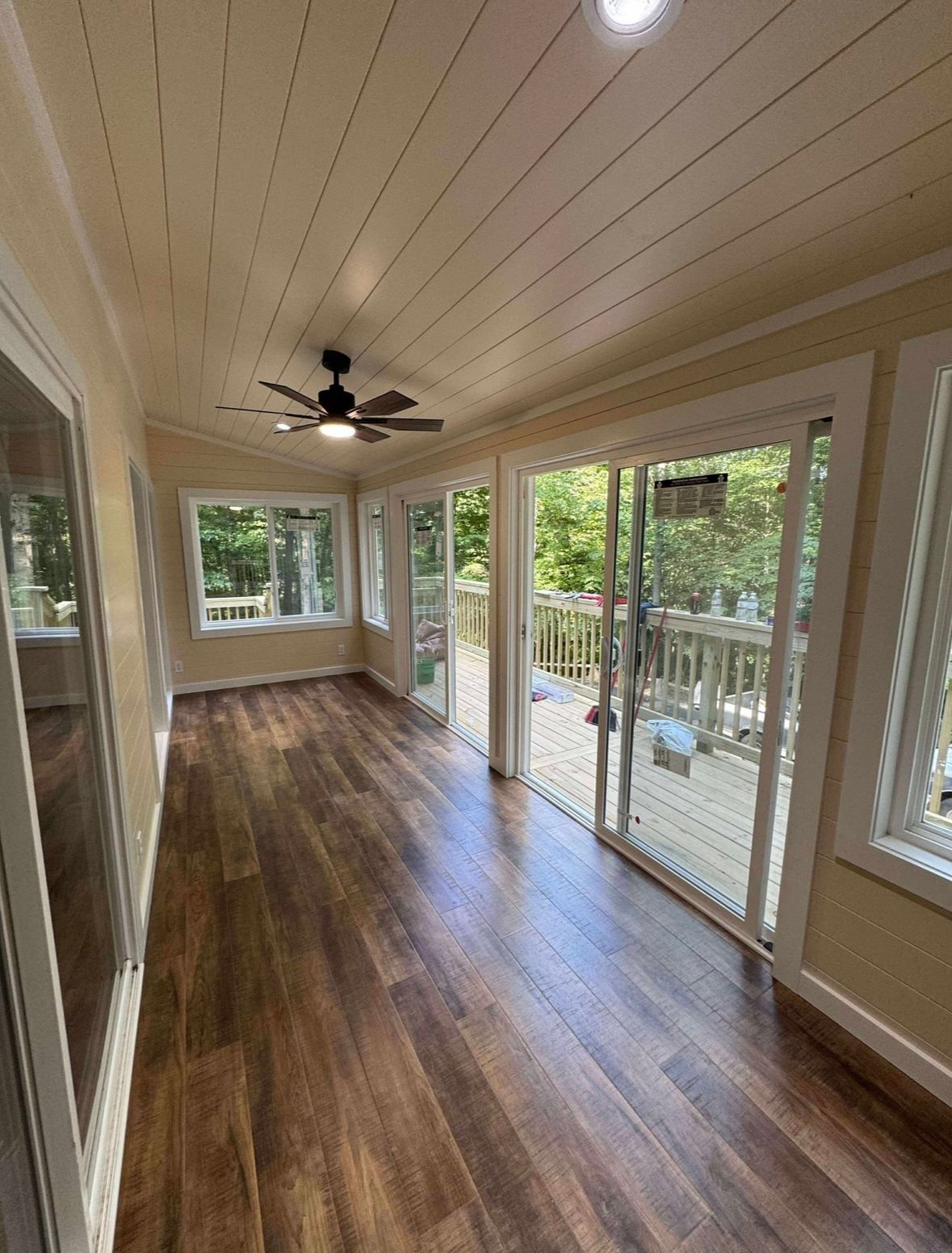 Bright sunroom with wood floors, white ceiling fan, and large windows overlooking greenery