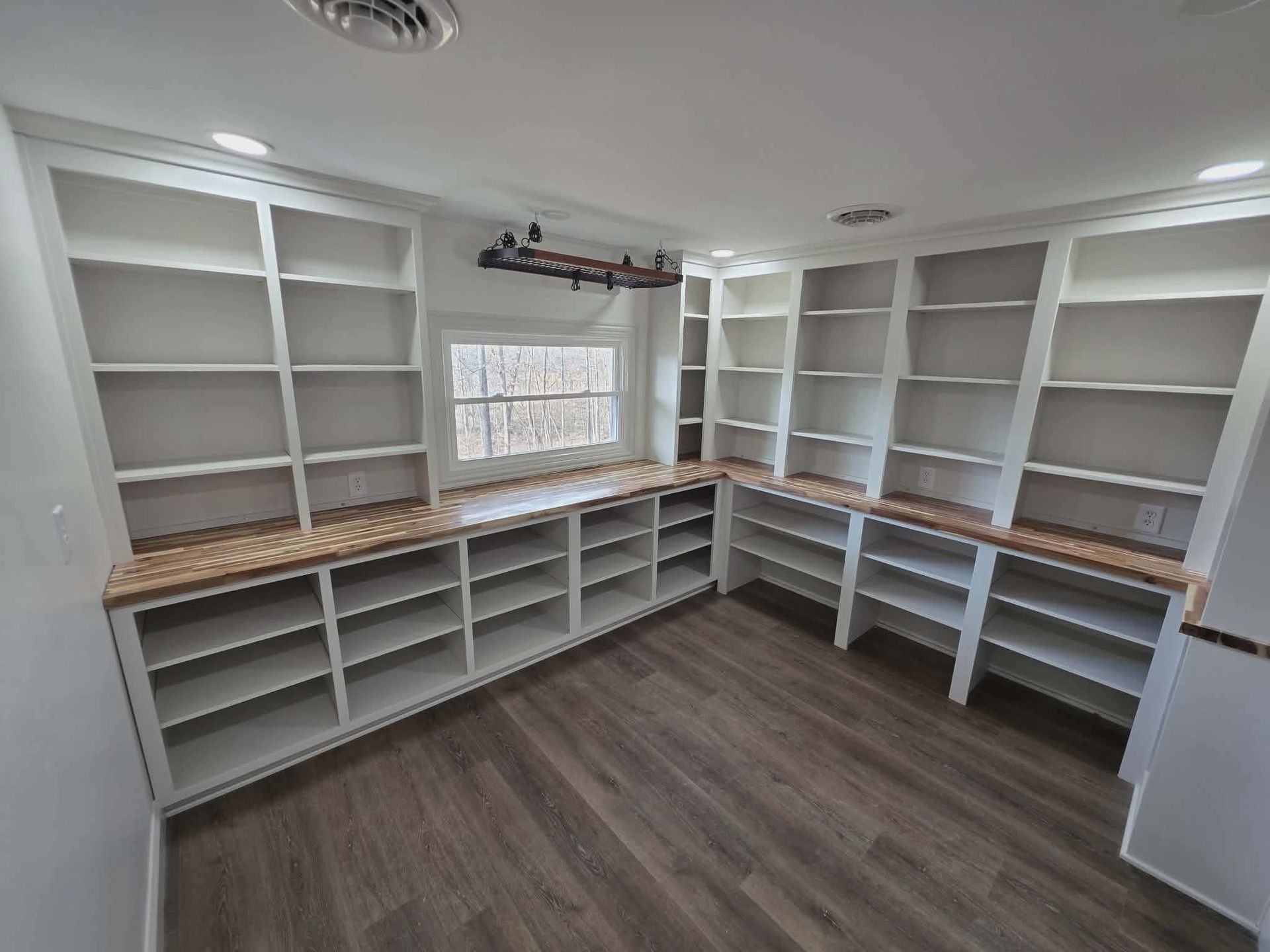 Built-in white shelving and cabinets in a bright walk-in closet with wood-look flooring