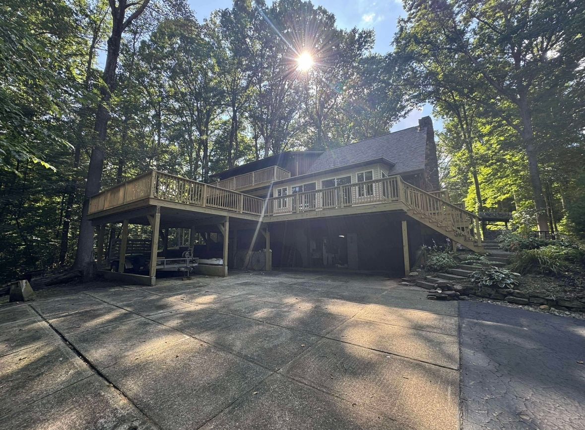 Wooden deck and stairs on a house in a wooded driveway, with sunlight filtering through trees.