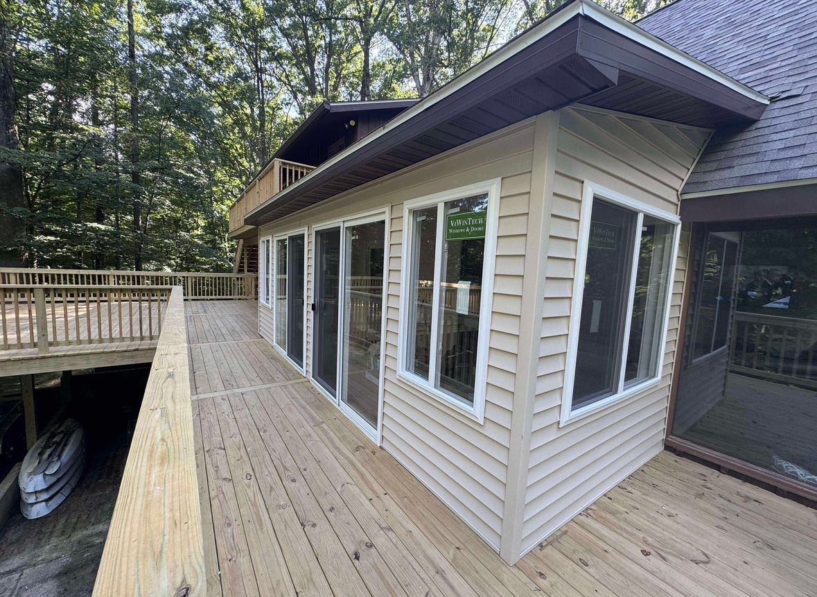 Wooden deck beside a beige house with large windows, surrounded by trees