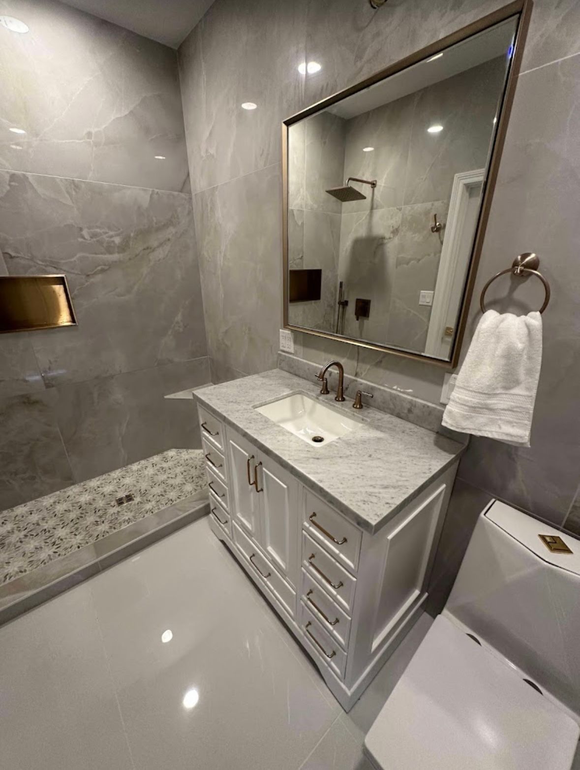 Modern bathroom with marble tile, vanity sink, large mirror, shower, and glossy floor.