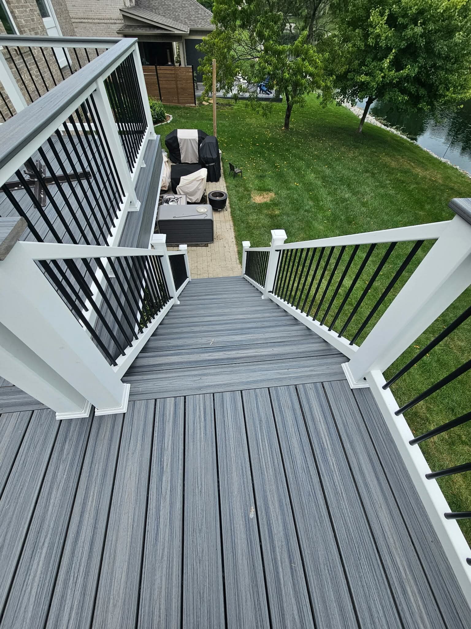 Deck stairs overlooking a grassy yard with patio furniture and a river beyond