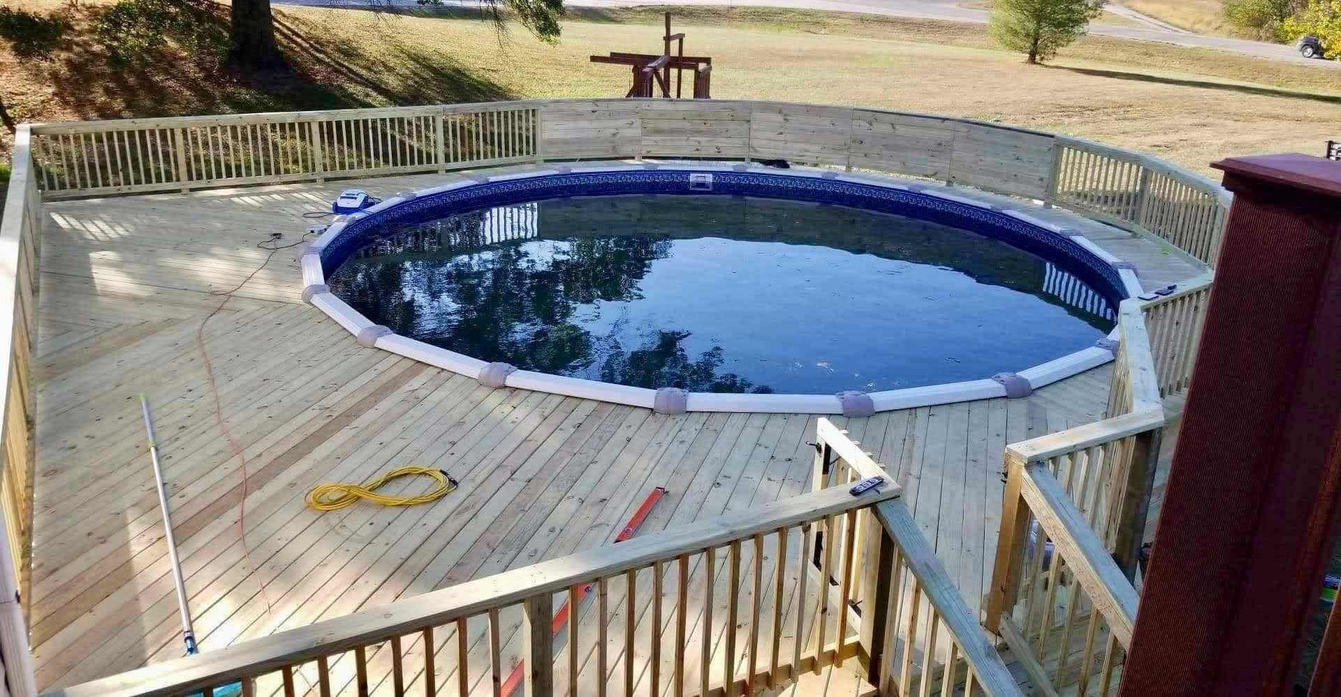 Round above-ground pool with blue cover on a wooden deck, surrounded by railings and yard grass.