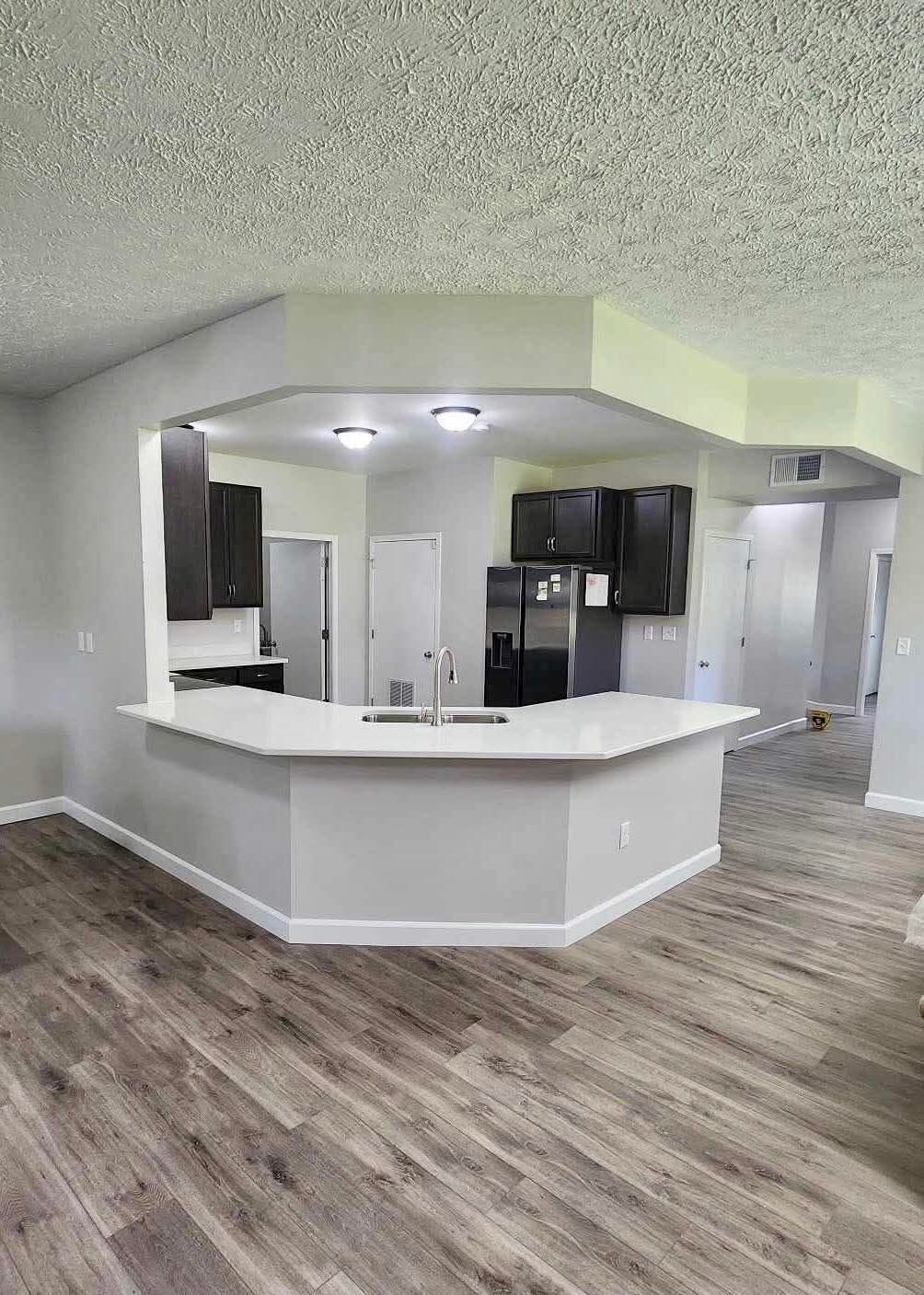 Empty modern kitchen with white island, dark cabinets, and wood-look flooring in an open-concept room