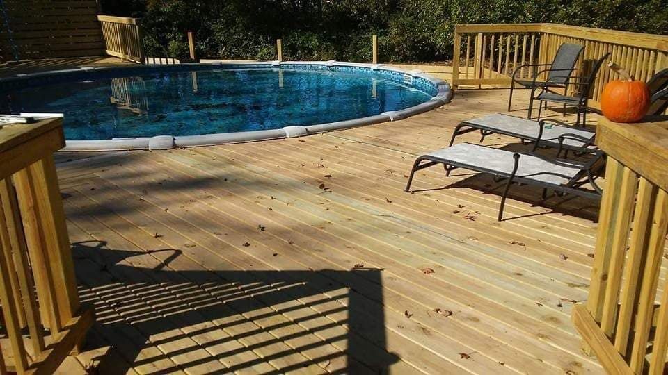 Wooden deck beside a blue above-ground pool with lounge chair and autumn leaves; pumpkin on railing.