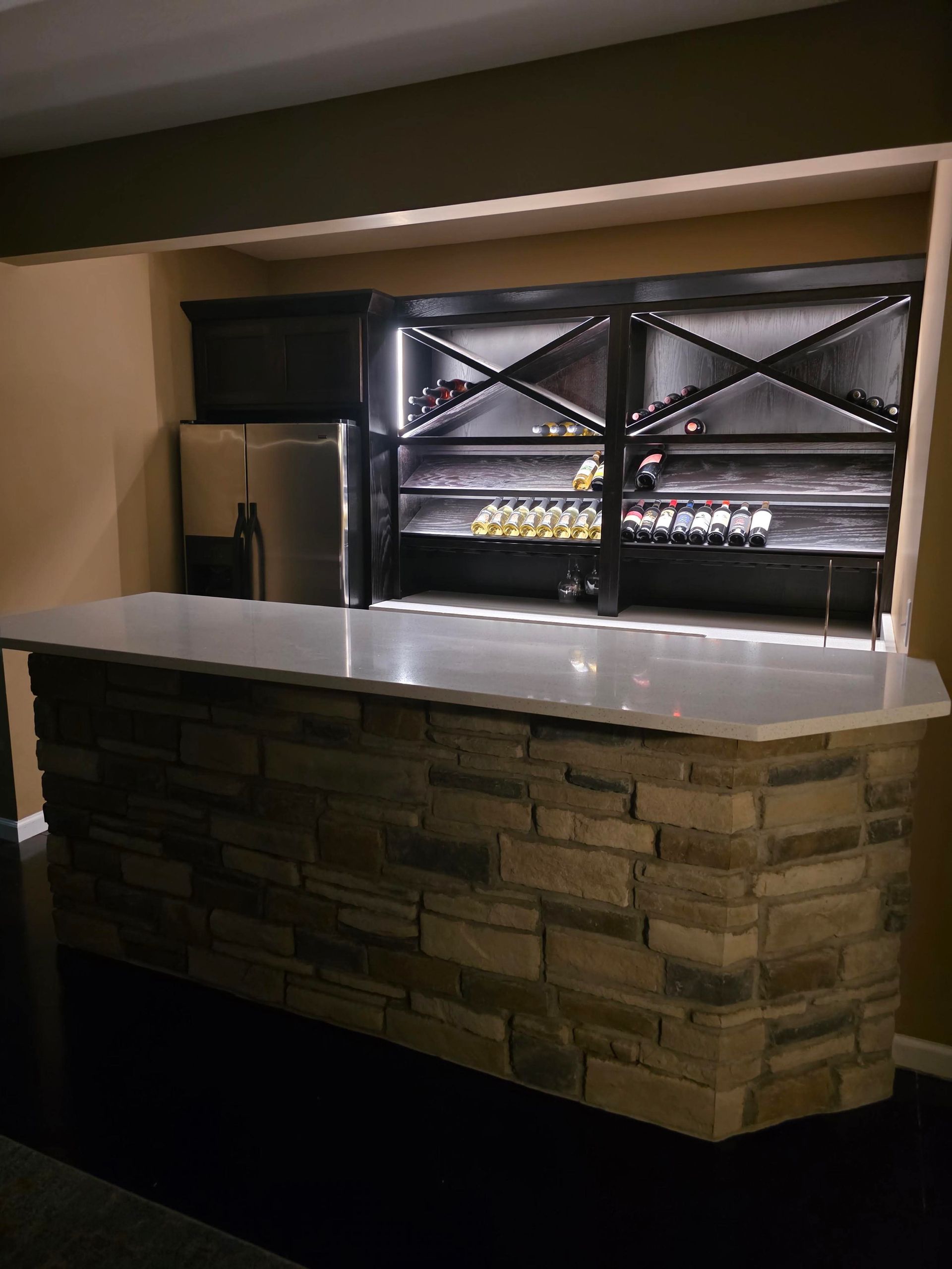 Stone-front bar counter with a stainless fridge and illuminated display case in a dim lounge.