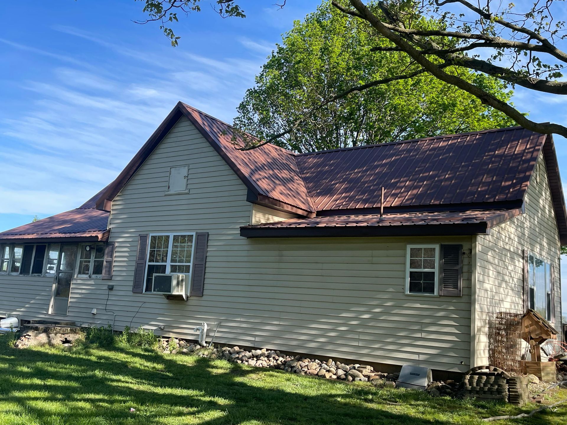 Side view of a white house with a red roof and a large tree in the yard under a blue sky