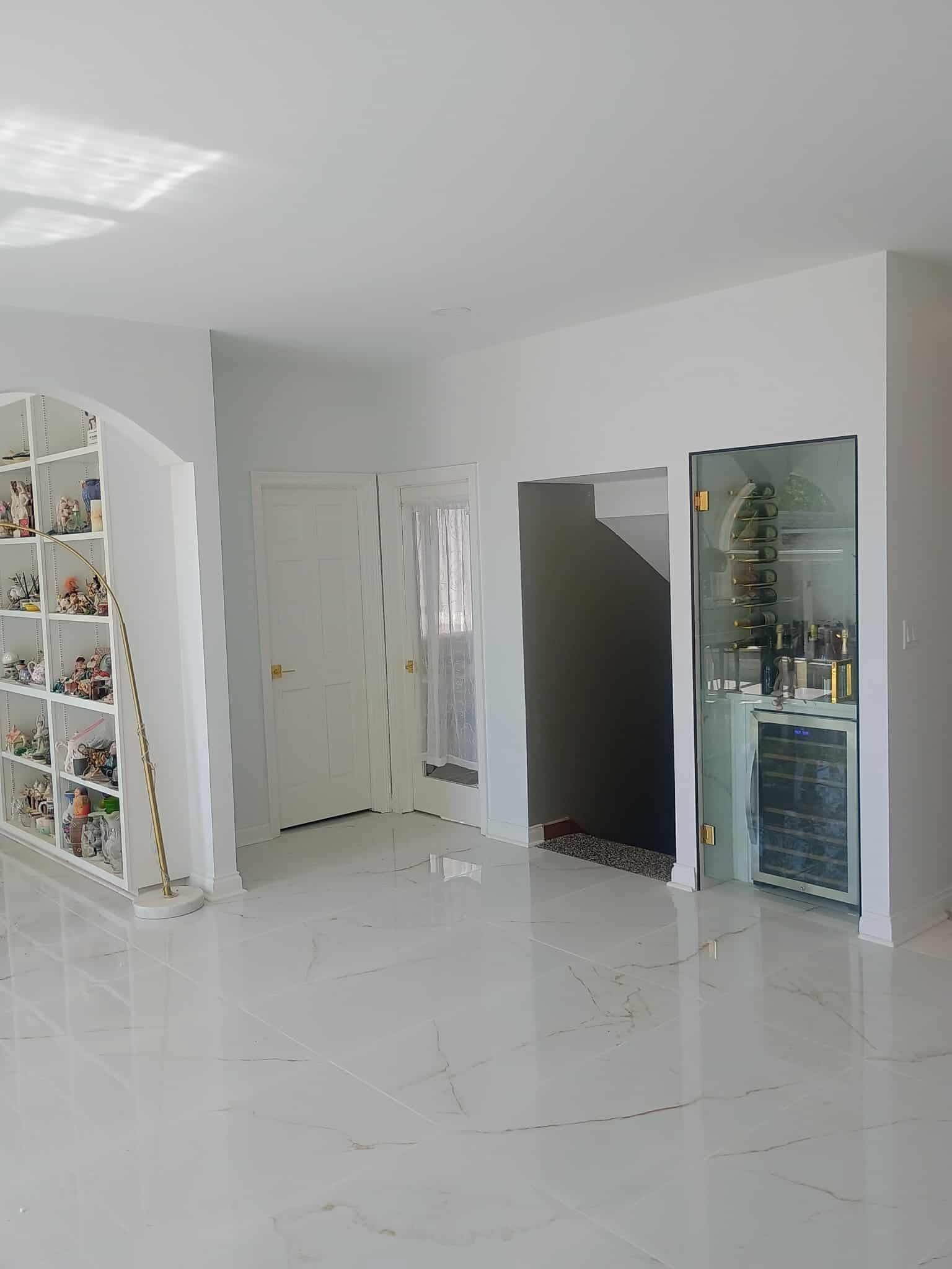 Bright white room with glossy tile floor, shelves, doors, and a glass display cabinet.