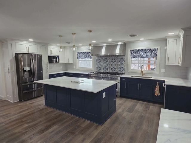 Modern kitchen with dark blue island, white countertops, stainless appliances, and wood flooring.