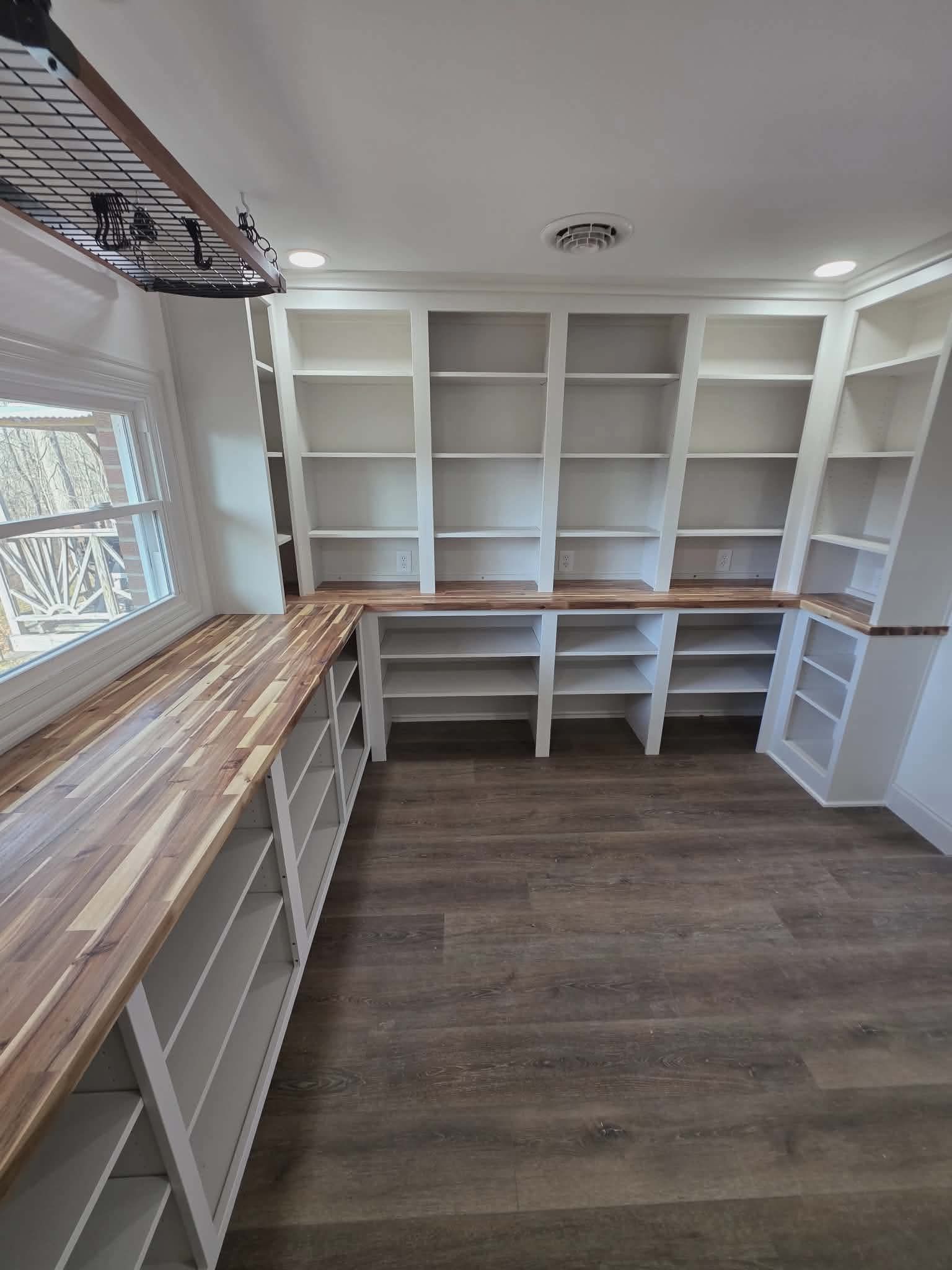 Empty walk-in closet with white shelving, wood floors, and a windowed counter area