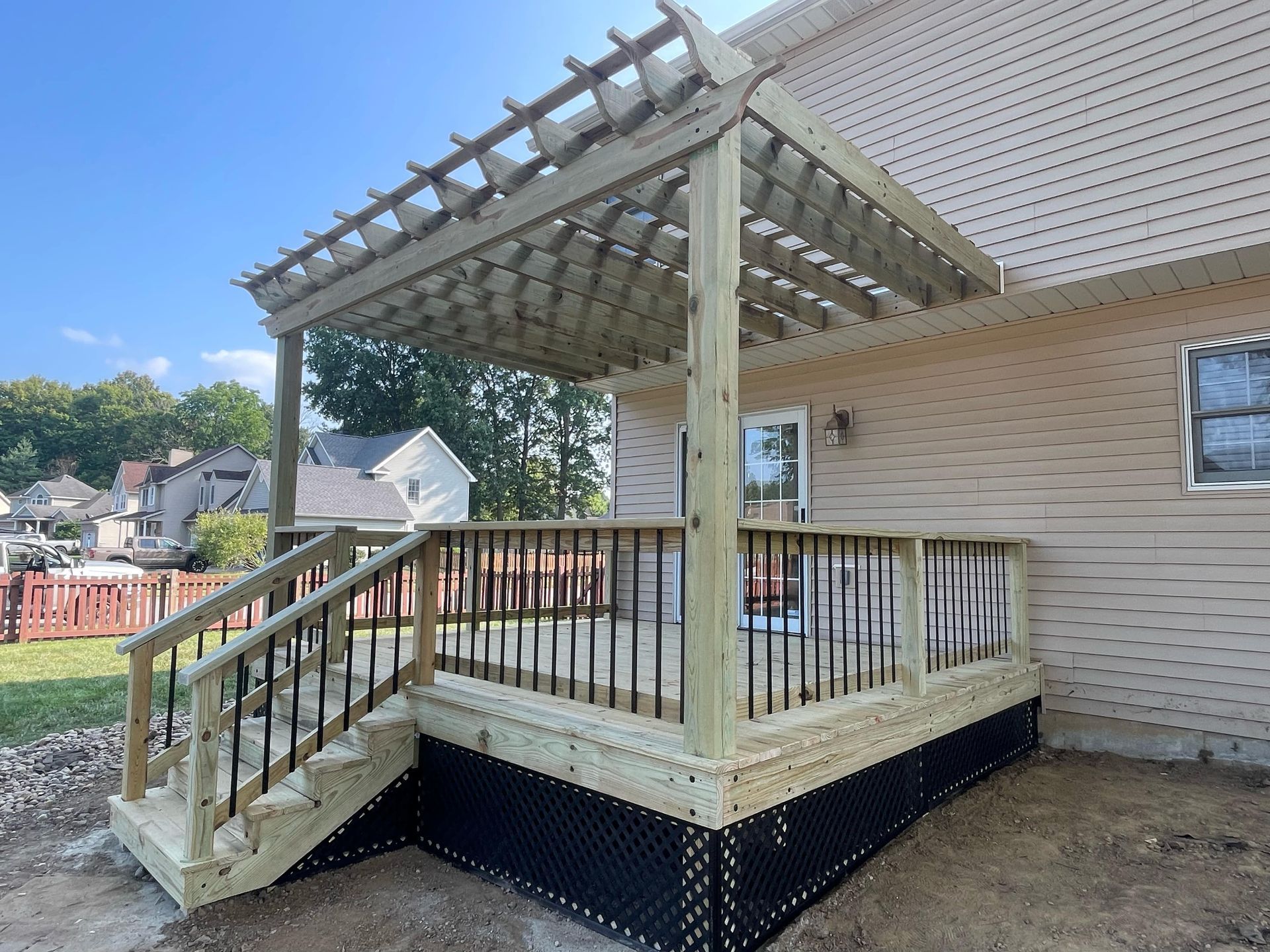 Wooden backyard deck with pergola and stairs beside a beige house.