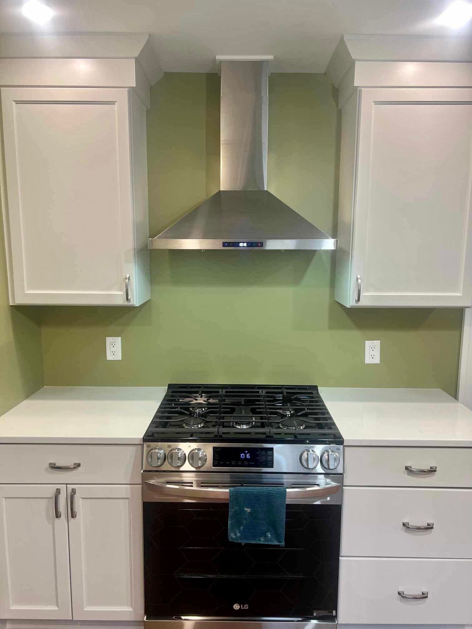 White kitchen with green walls, stainless steel range hood, black stove, and white cabinets.