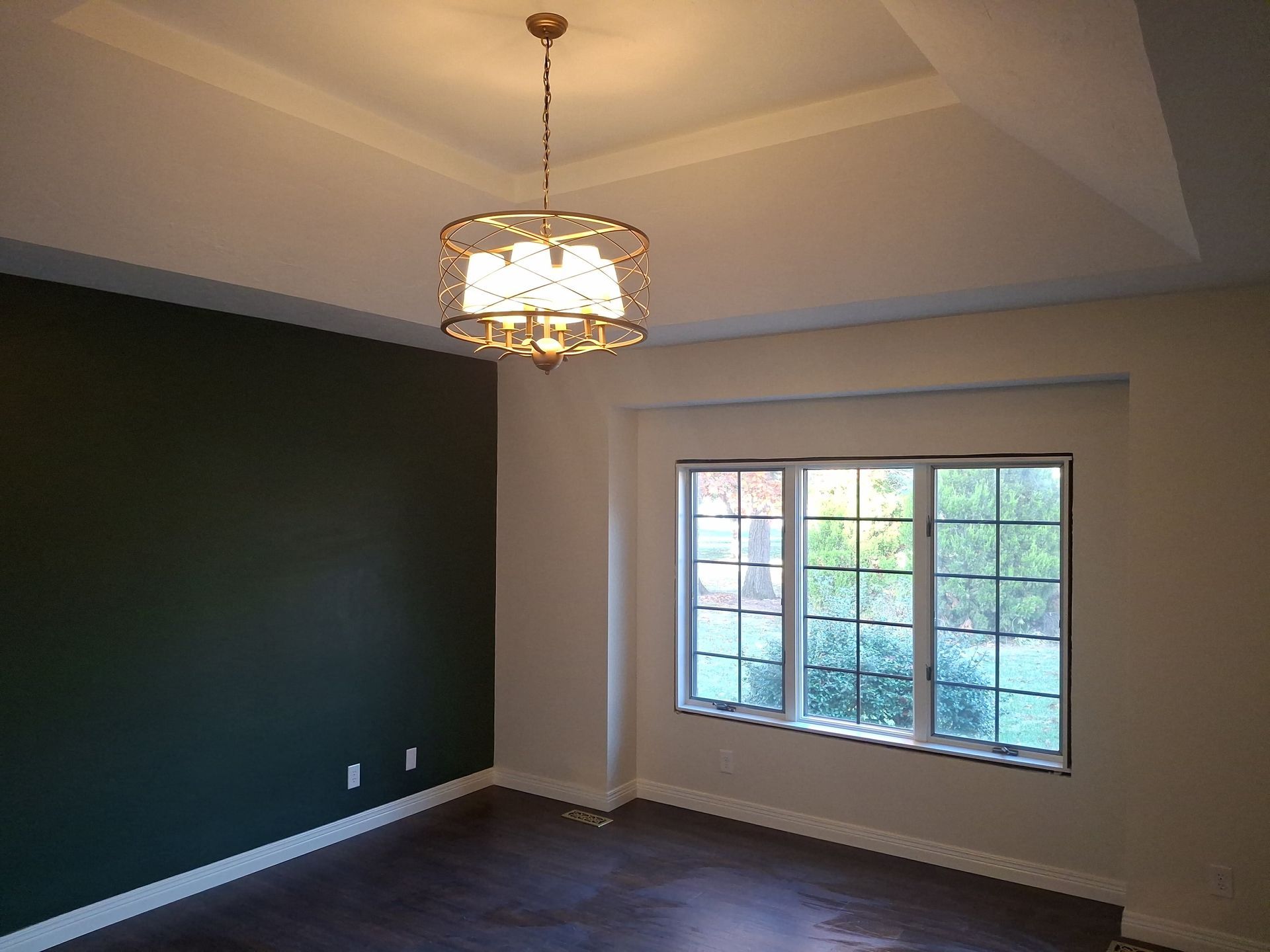 Empty room with dark green accent wall, chandelier, and large window with blinds