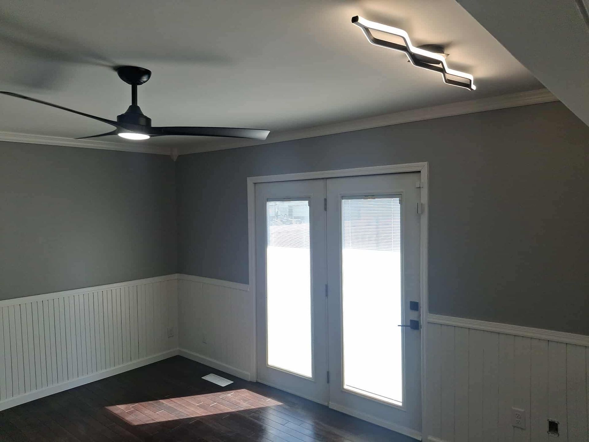 Empty gray room with white wainscoting, ceiling fan, and double glass doors