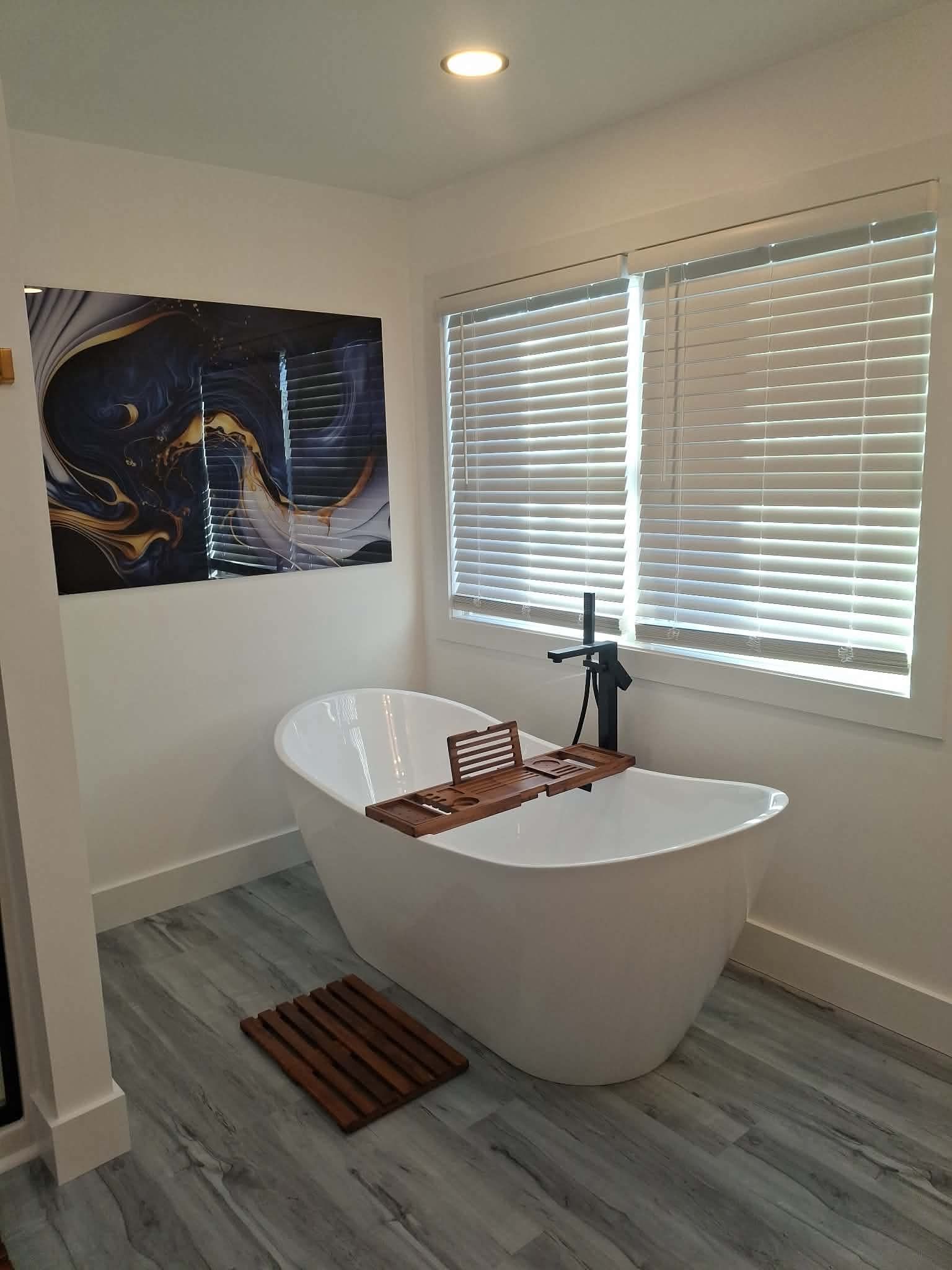 Modern bathroom with a white freestanding tub, window blinds, gray floor, and abstract wall art
