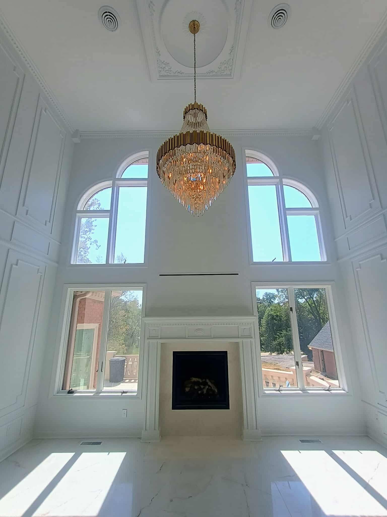 Elegant white room with tall arched windows, crystal chandelier, and central fireplace.