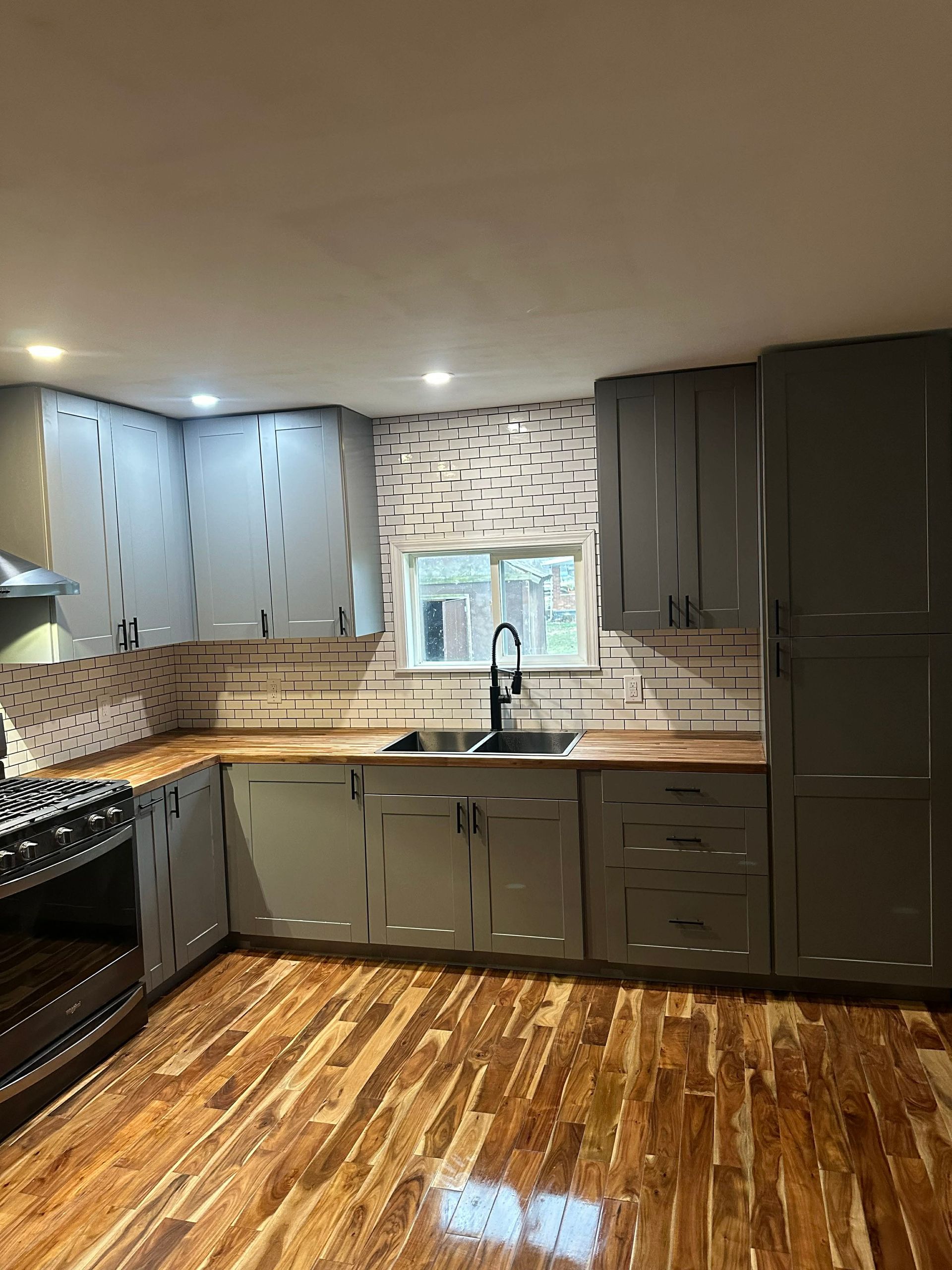 Modern kitchen with dark cabinets, patterned backsplash, stainless appliances, and wood floors