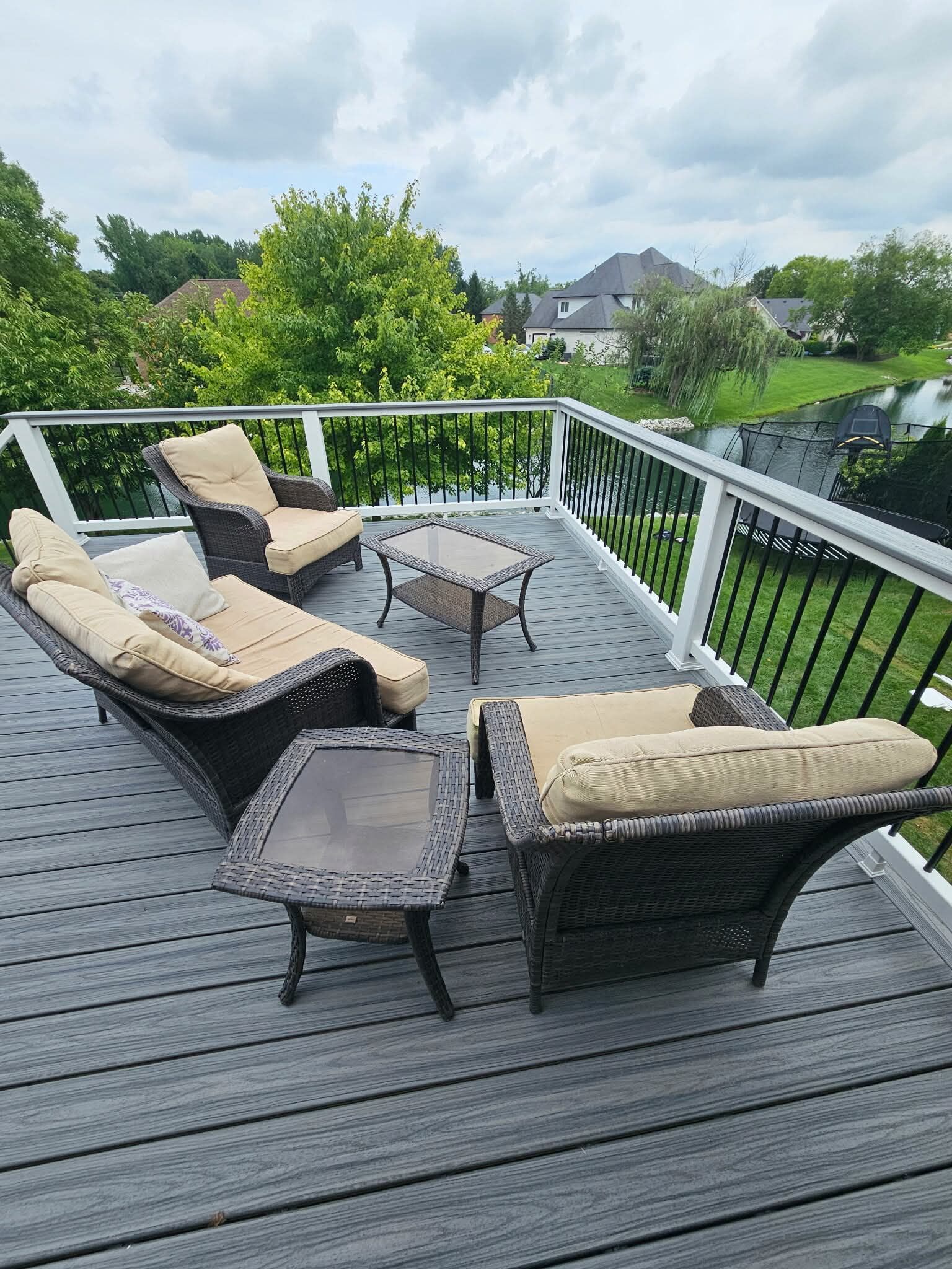 Patio deck with wicker chairs and table overlooking a green backyard and houses