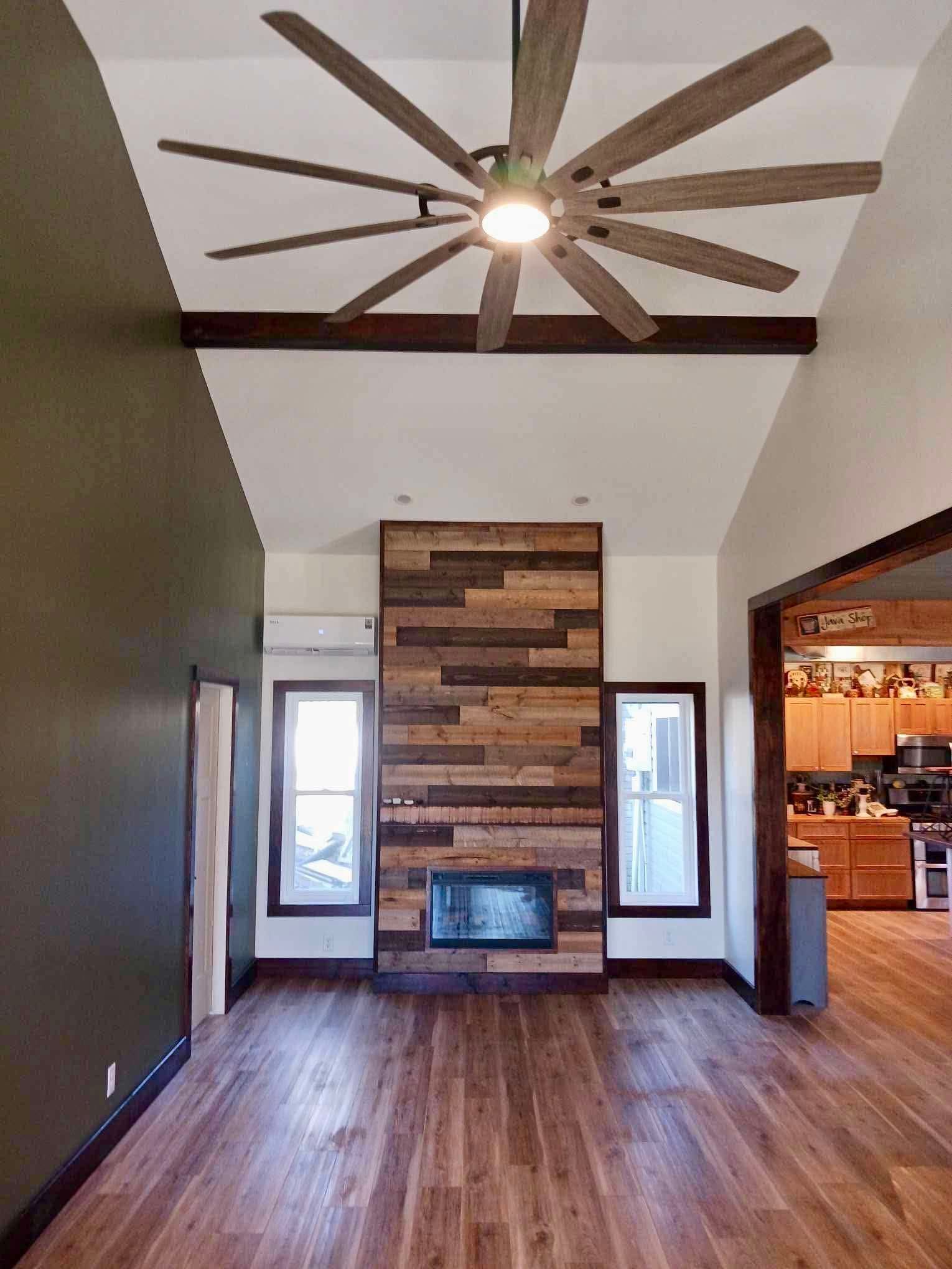 Empty living room with wood floor, vaulted ceiling fan, and stone fireplace centered between windows