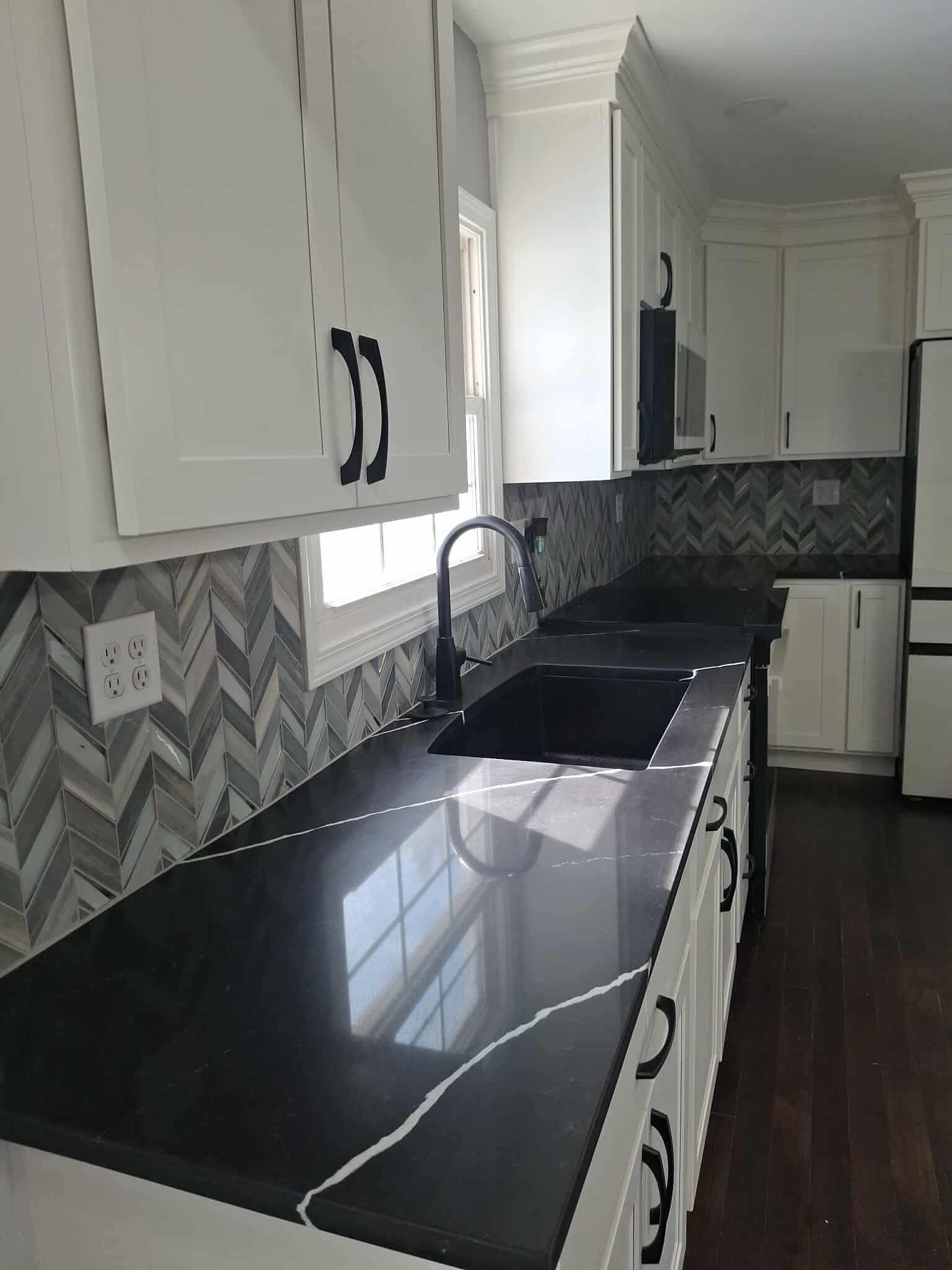 Modern kitchen with white cabinets, black countertops, herringbone backsplash, and a sink by the window