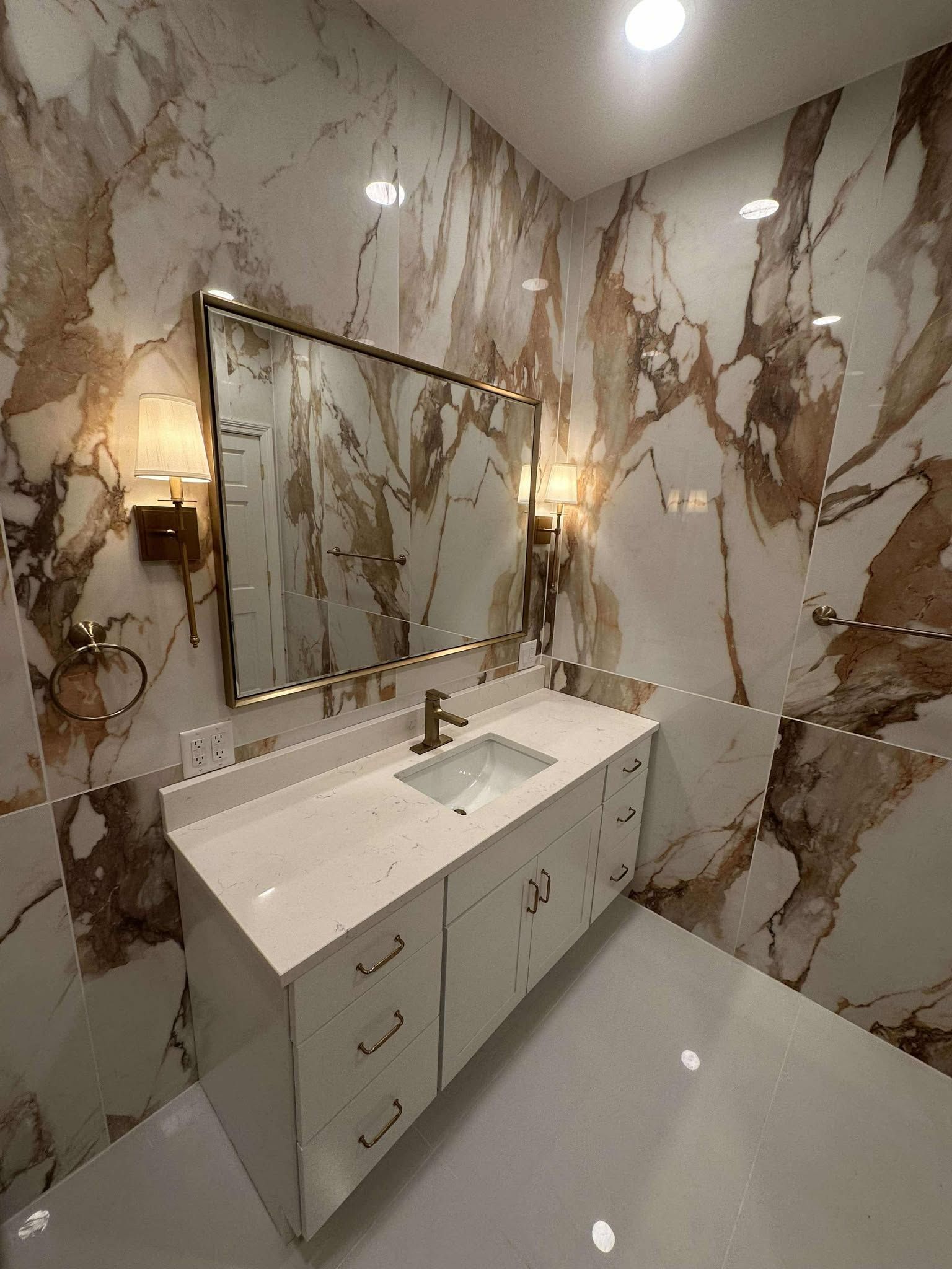 Elegant marble bathroom with white vanity, large gold-framed mirror, and wall sconce lighting.