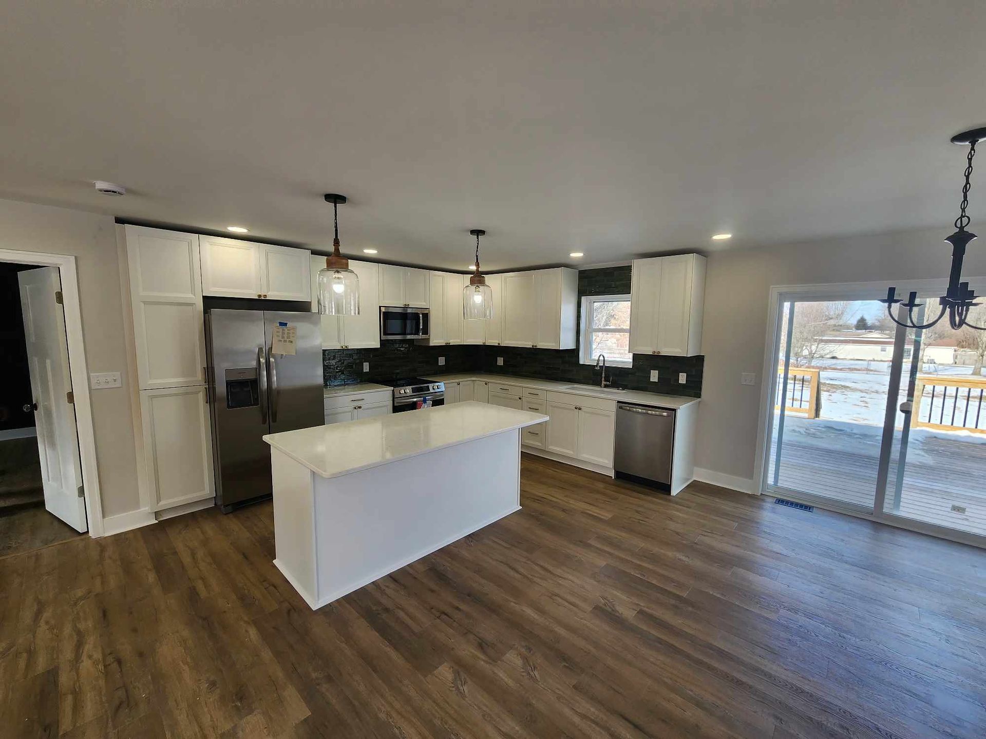 Open-plan kitchen with white island, dark floors, stainless appliances, and sliding glass doors.