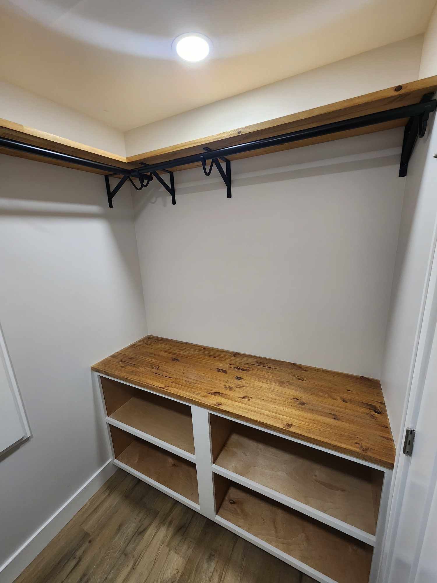 Small walk-in closet with wooden shelves, hanging rods, and a wood countertop over open cubbies.