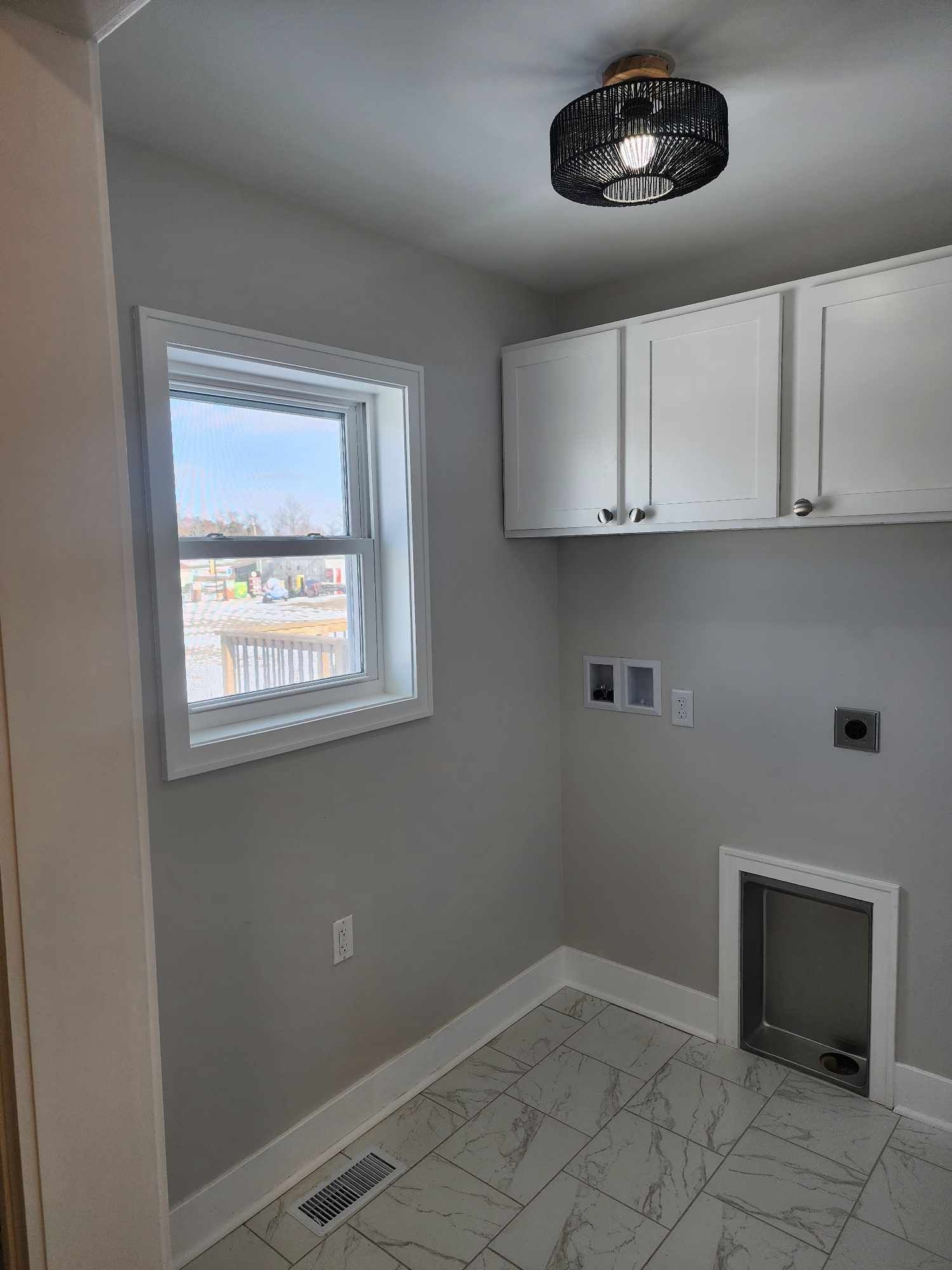 Small laundry room with white cabinets, window, tiled floor, and a utility hookup on the wall.